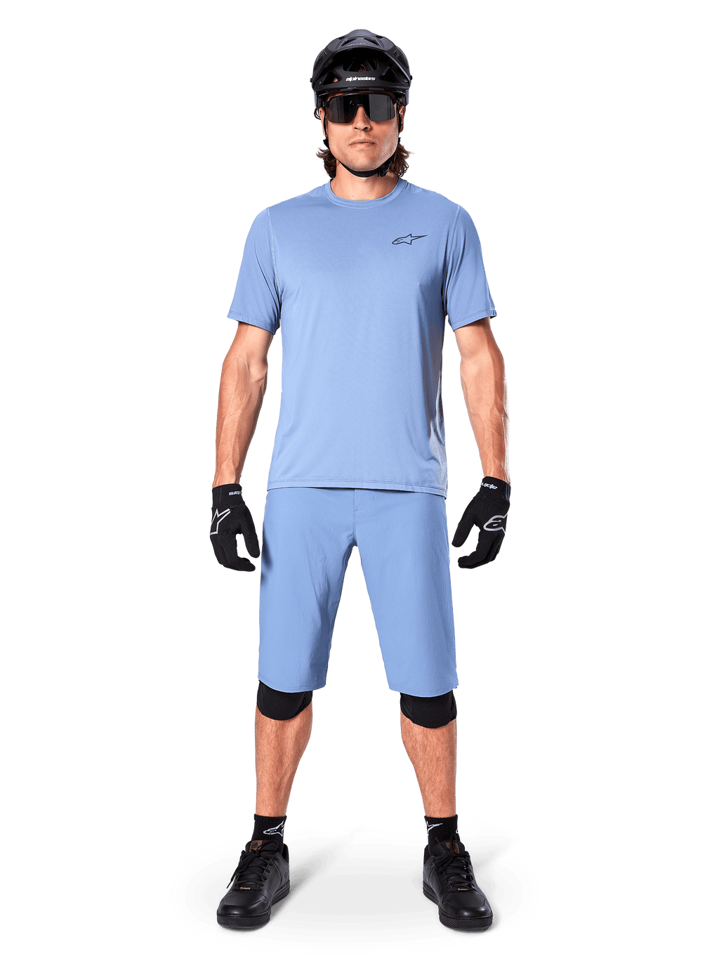 Modell som bär Alpinestars A-Dura Shorts i Infinity Blue, matchande ljusblå tröja, svart mountainbikehjälm, svarta solglasögon, svarta handskar och knäskydd, komplett MTB-outfit för trailcykling