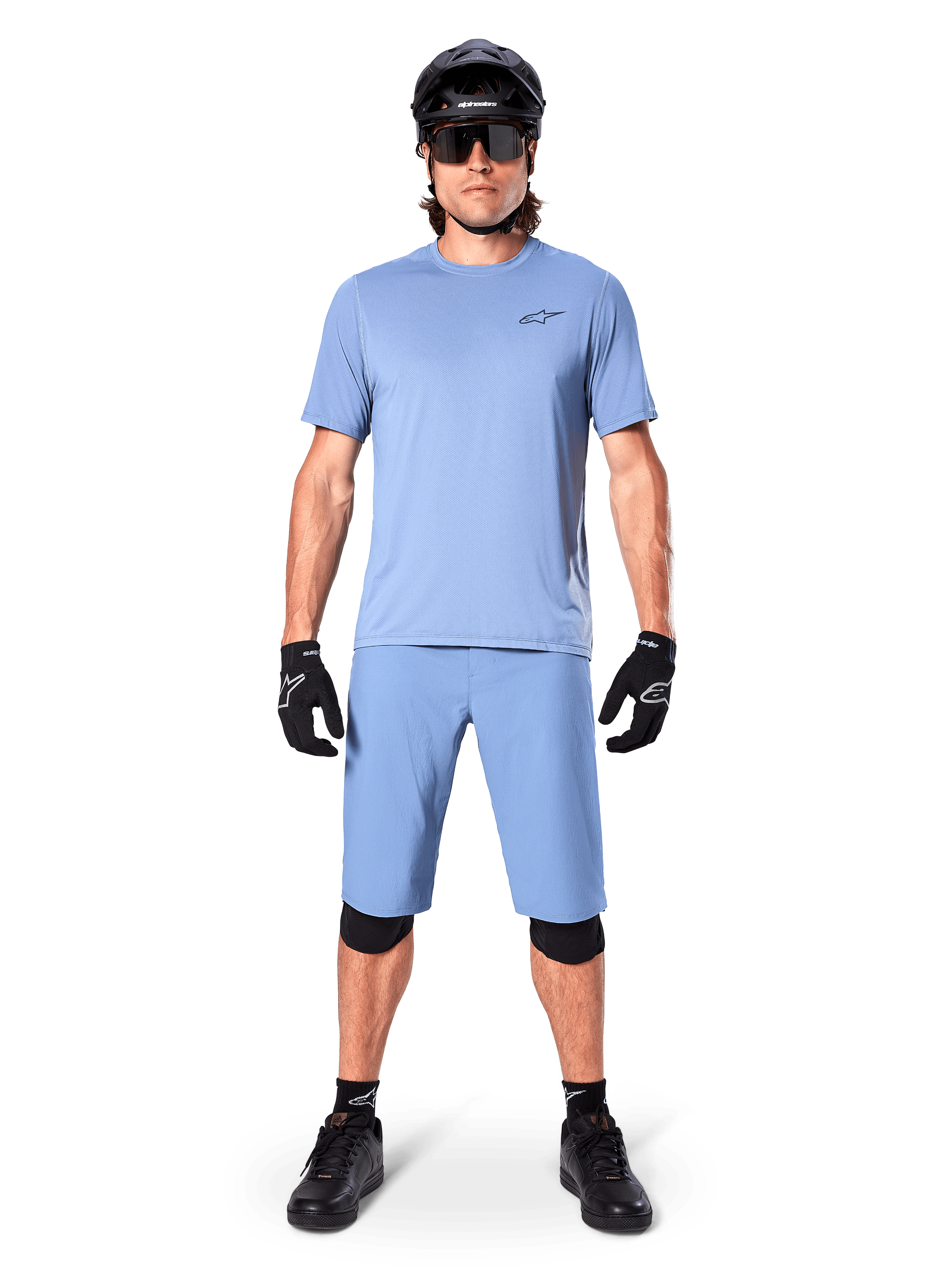 Modell som bär Alpinestars A-Dura Shorts i Infinity Blue, matchande ljusblå tröja, svart mountainbikehjälm, svarta solglasögon, svarta handskar och knäskydd, komplett MTB-outfit för trailcykling