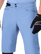 Alpinestars A-Dura Shorts, Infinity Blue mountainbikeshorts, närbild på midjan med dubbelknäppning, justerbart sidoreglage och dragkedjeförsedda nätfodrade fickor, bärs med en svart Alpinestars-handske