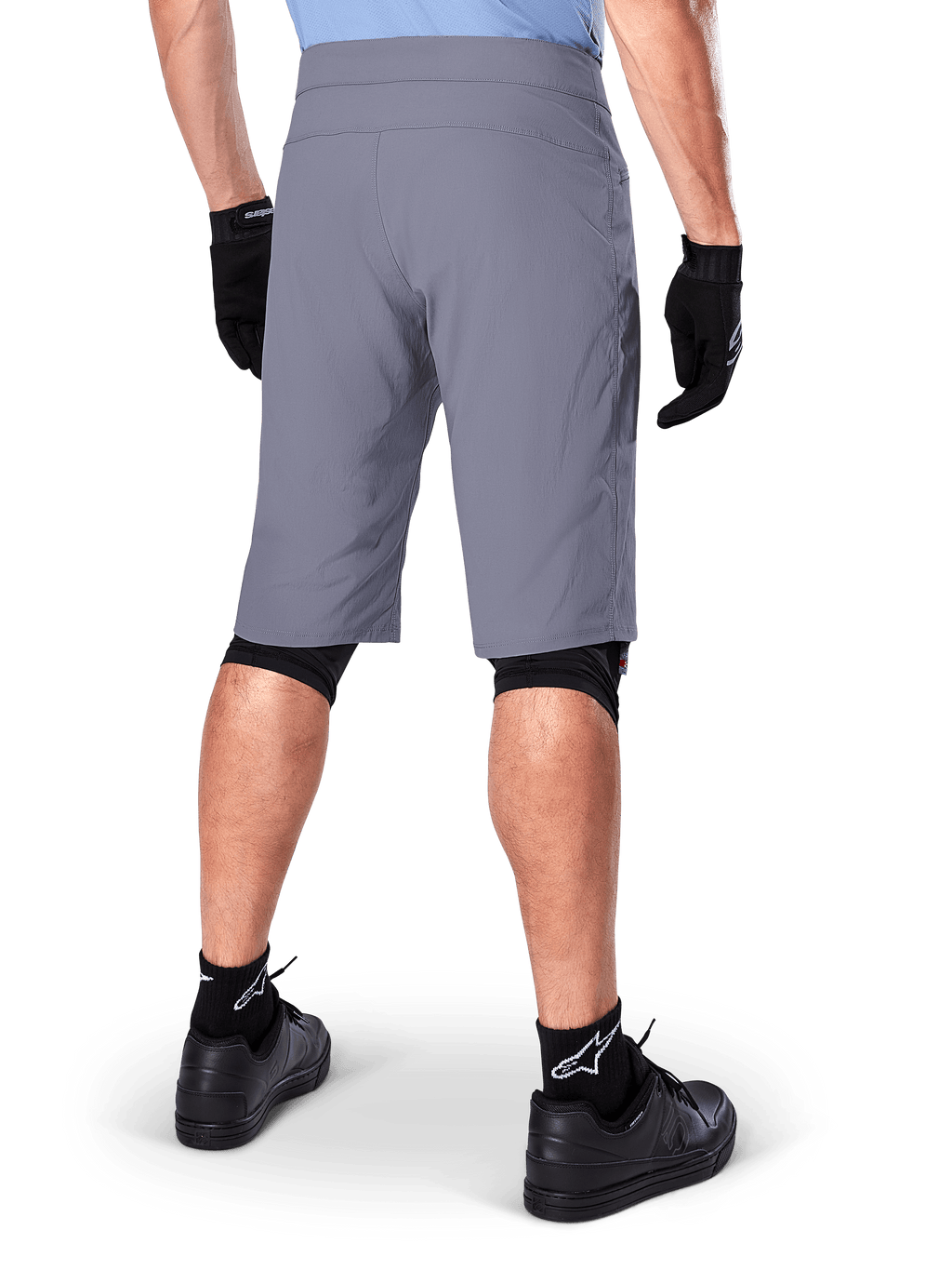 Alpinestars A-Dura Shorts, mörkgrå mountainbikeshorts, sedda bakifrån på en åkare, bärs med svarta handskar, svarta knäskyddsfoder och svarta strumpor med Alpinestars-logotyp, slitstark konstruktion för terrängcykling
