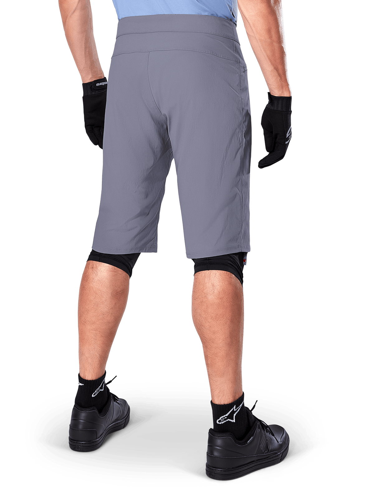 Alpinestars A-Dura Shorts, mörkgrå mountainbikeshorts, sedda bakifrån på en åkare, bärs med svarta handskar, svarta knäskyddsfoder och svarta strumpor med Alpinestars-logotyp, slitstark konstruktion för terrängcykling