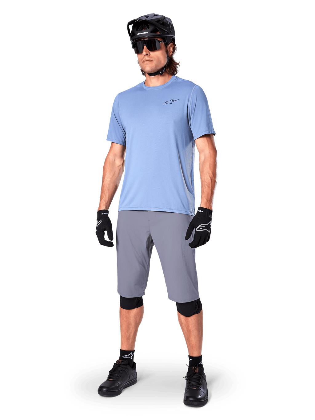 Alpinestars A-Dura shorts, MTB-shorts, mörkgrå, bärs av en cyklist med en ljusblå tröja, svart MTB-hjälm, svarta handskar och knäskydd, komplett mountainbikeoutfit för trail- och terrängkörning