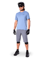 Alpinestars A-Dura shorts, MTB-shorts, mörkgrå, bärs av en cyklist med en ljusblå tröja, svart MTB-hjälm, svarta handskar och knäskydd, komplett mountainbikeoutfit för trail- och terrängkörning