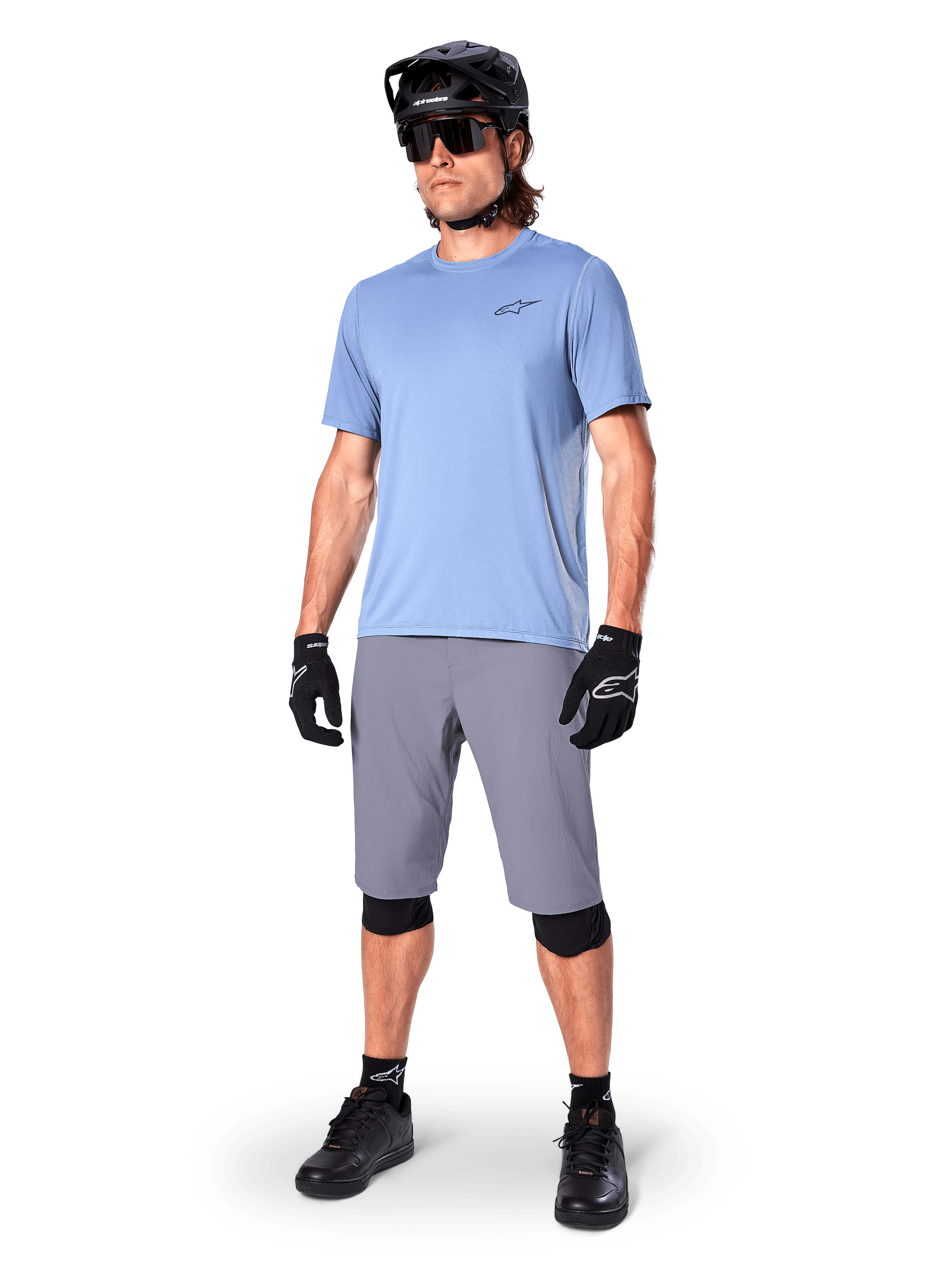 Alpinestars A-Dura shorts, MTB-shorts, mörkgrå, bärs av en cyklist med en ljusblå tröja, svart MTB-hjälm, svarta handskar och knäskydd, komplett mountainbikeoutfit för trail- och terrängkörning
