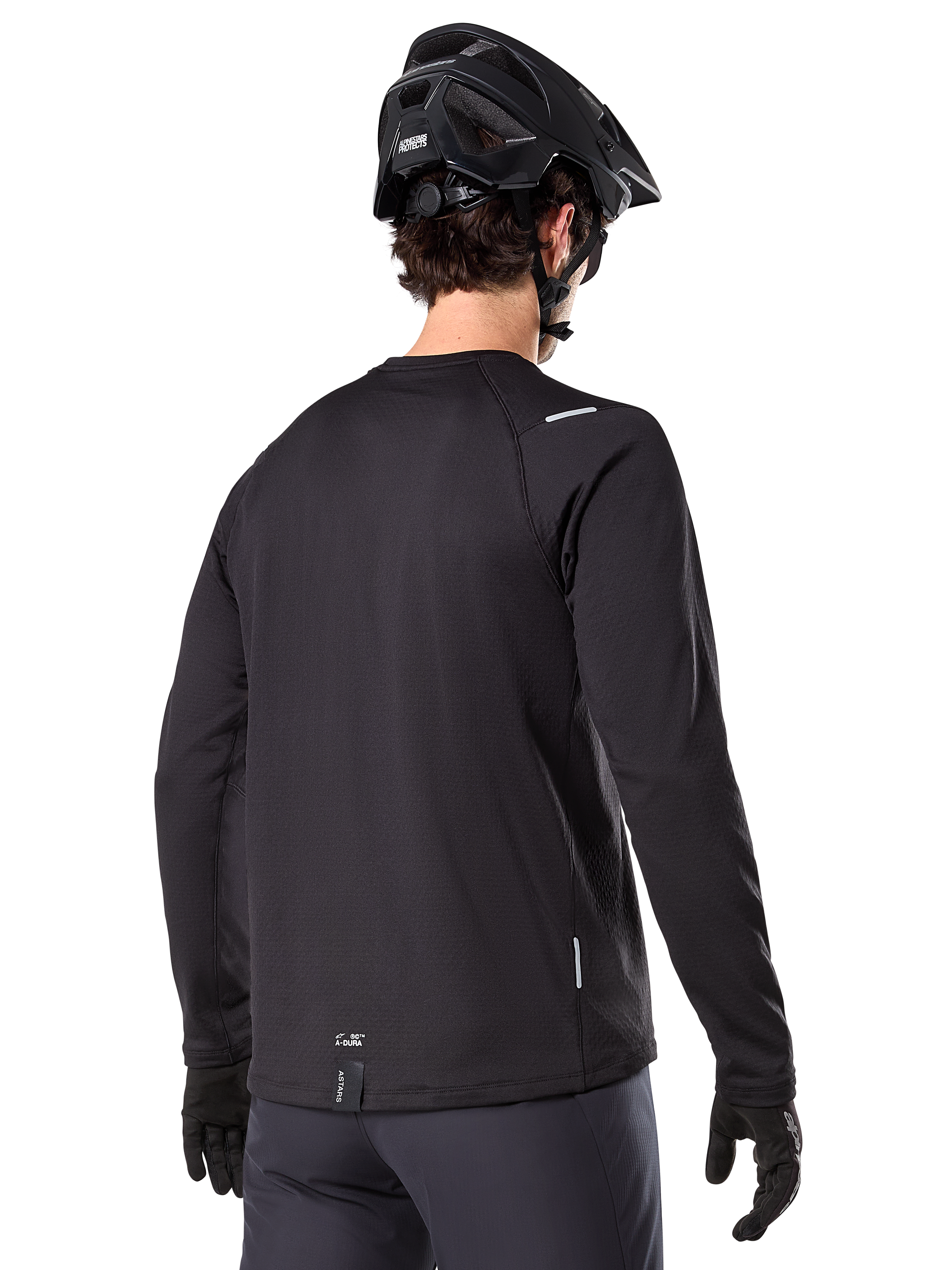 Alpinestars A-Dura Thermal Tröja, långärmad mountainbiketröja, svart, vy bakifrån som visar förlängt bakstycke, små reflekterande detaljer och logotyp vid fållen, bärs med svart hjälm och handskar för cykling i kallt väder