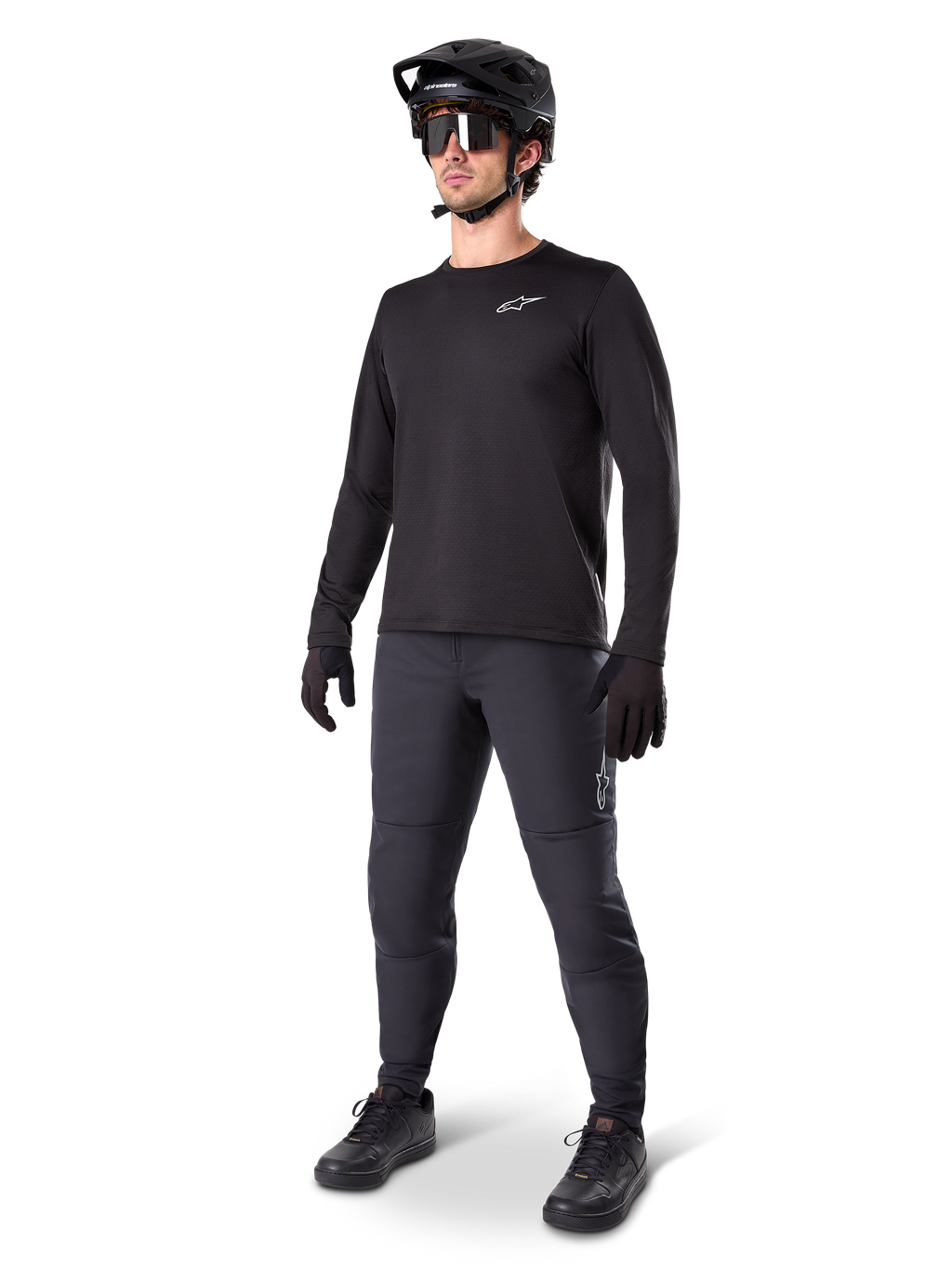 Modell som bär Alpinestars A-Dura Thermal Tröja, svart långärmad MTB-tröja, svart mountainbikehjälm, solglasögon och mörkgrå byxor, med en liten vit logotyp på bröstet, isolerande fleecekonstruktion för cykling i kallt väder