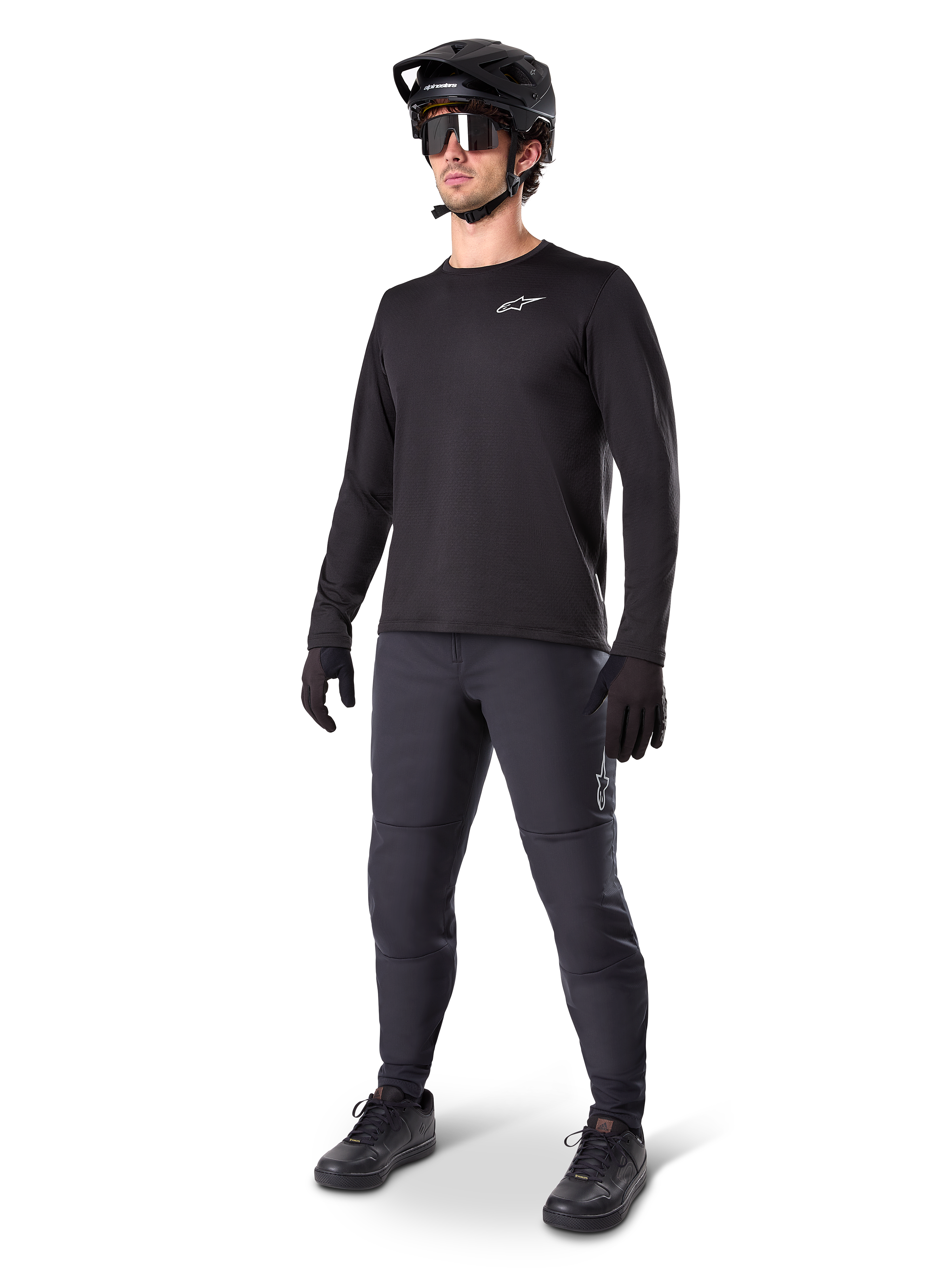 Modell som bär Alpinestars A-Dura Thermal Tröja, svart långärmad MTB-tröja, svart mountainbikehjälm, solglasögon och mörkgrå byxor, med en liten vit logotyp på bröstet, isolerande fleecekonstruktion för cykling i kallt väder