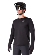Alpinestars A-Dura Thermal Jersey, svart långärmad mountainbiketröja, vit logotyp på bröstet, bärs med svart hjälm och handskar, stilren sportig design för trailcykling