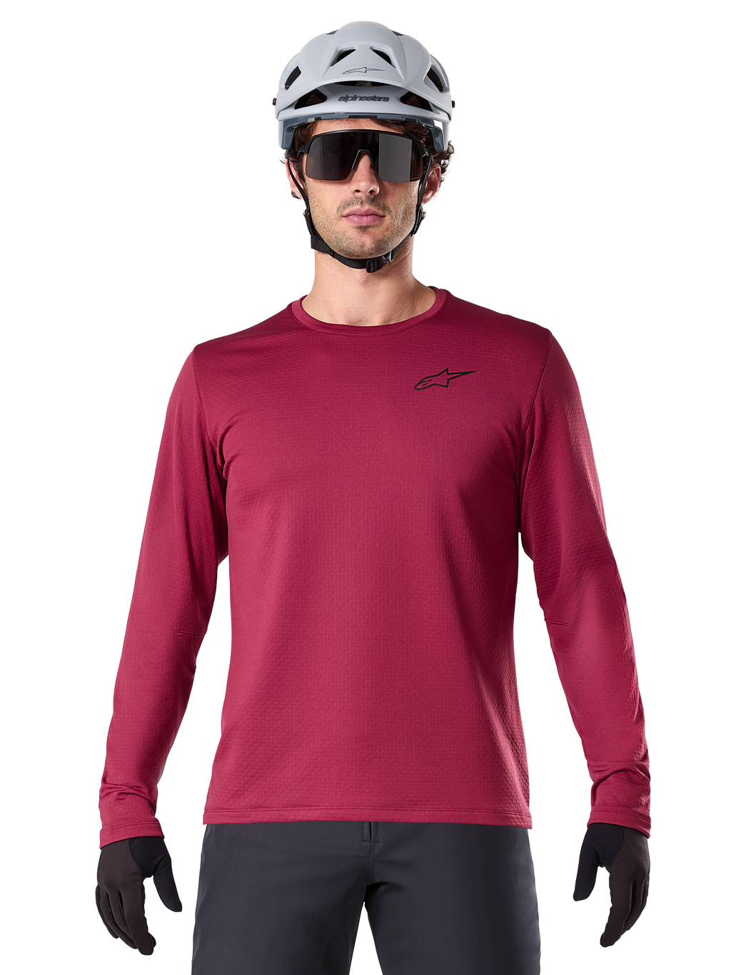 Manlig cyklist som bär Alpinestars A-Dura Thermal Jersey, långärmad MTB-tröja, vinröd, matchad med en grå hjälm och svarta solglasögon, har en liten svart stjärnlogotyp på bröstet, isolerat fleecetyg för mountainbike-turer i kallt väder