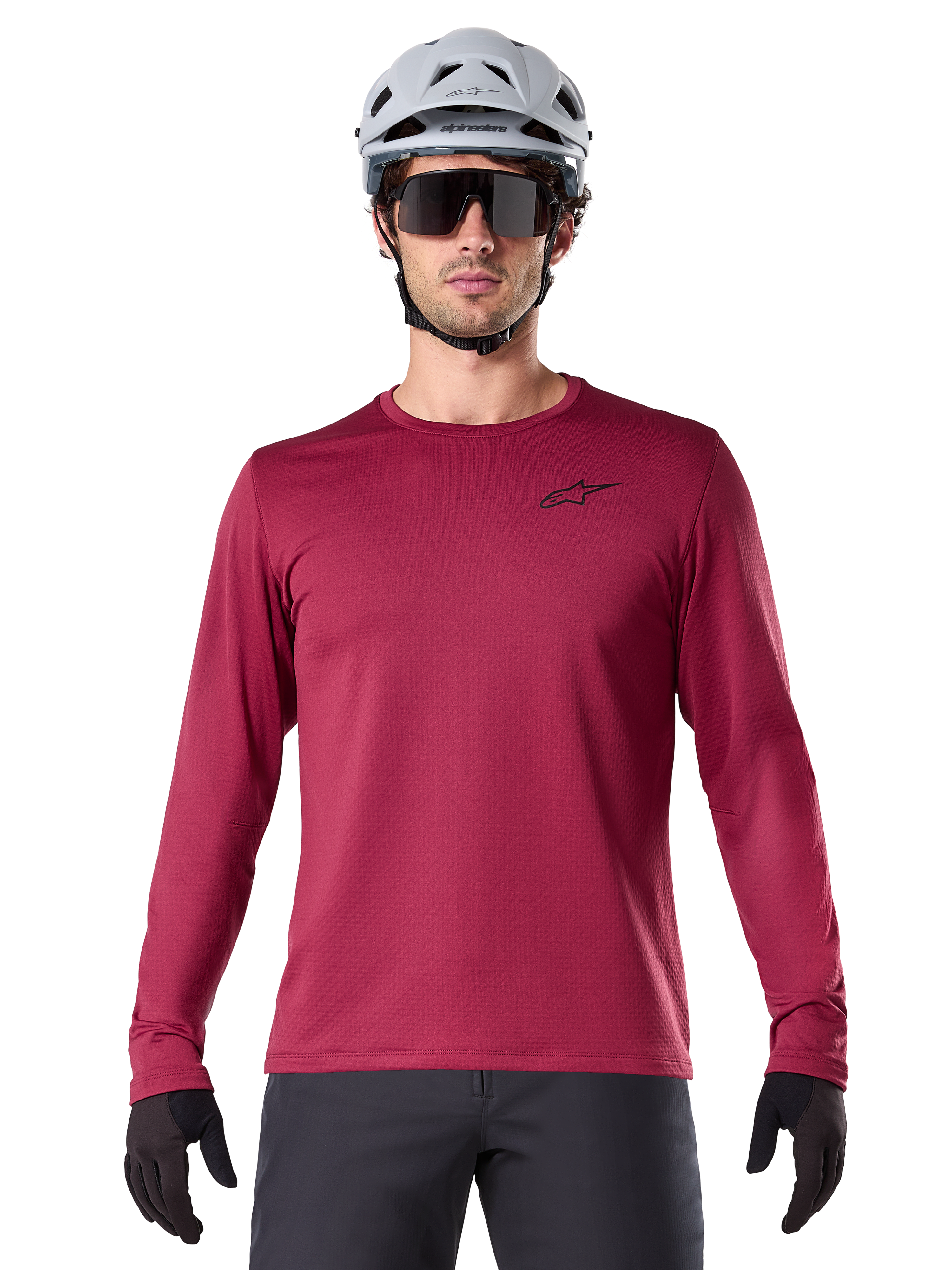 Manlig cyklist som bär Alpinestars A-Dura Thermal Jersey, långärmad MTB-tröja, vinröd, matchad med en grå hjälm och svarta solglasögon, har en liten svart stjärnlogotyp på bröstet, isolerat fleecetyg för mountainbike-turer i kallt väder
