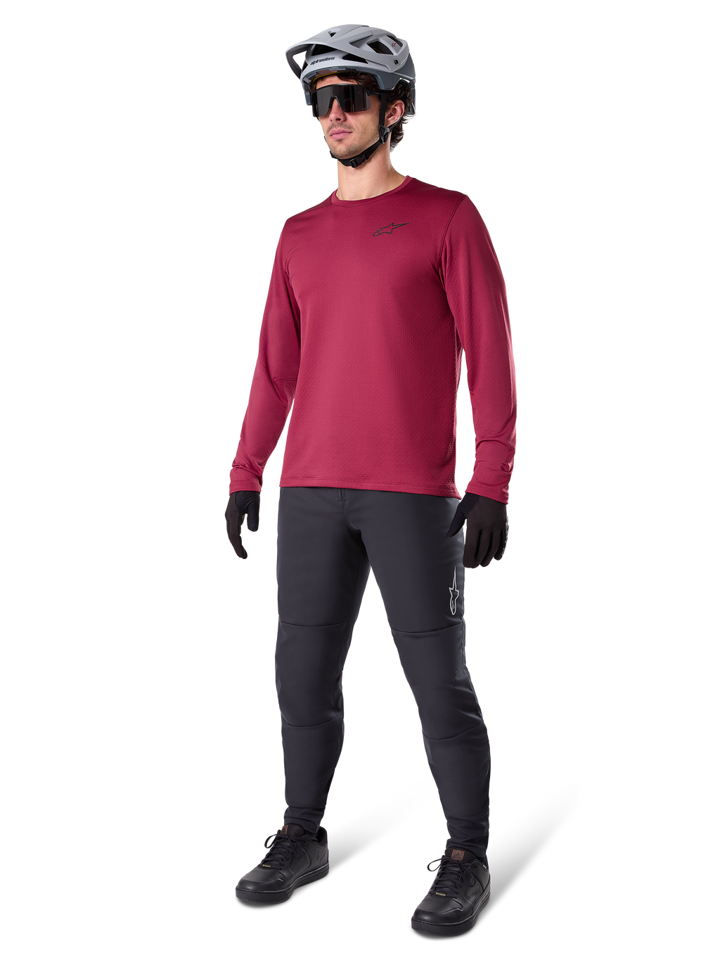 Alpinestars A-Dura Thermal Jersey i vinrött, långärmad isolerad cykeltröja bärs med mörkgrå mountainbikebyxor, svarta handskar och en grå hjälm, helkroppsbild i studio av MTB-utrustning för kallt väder.