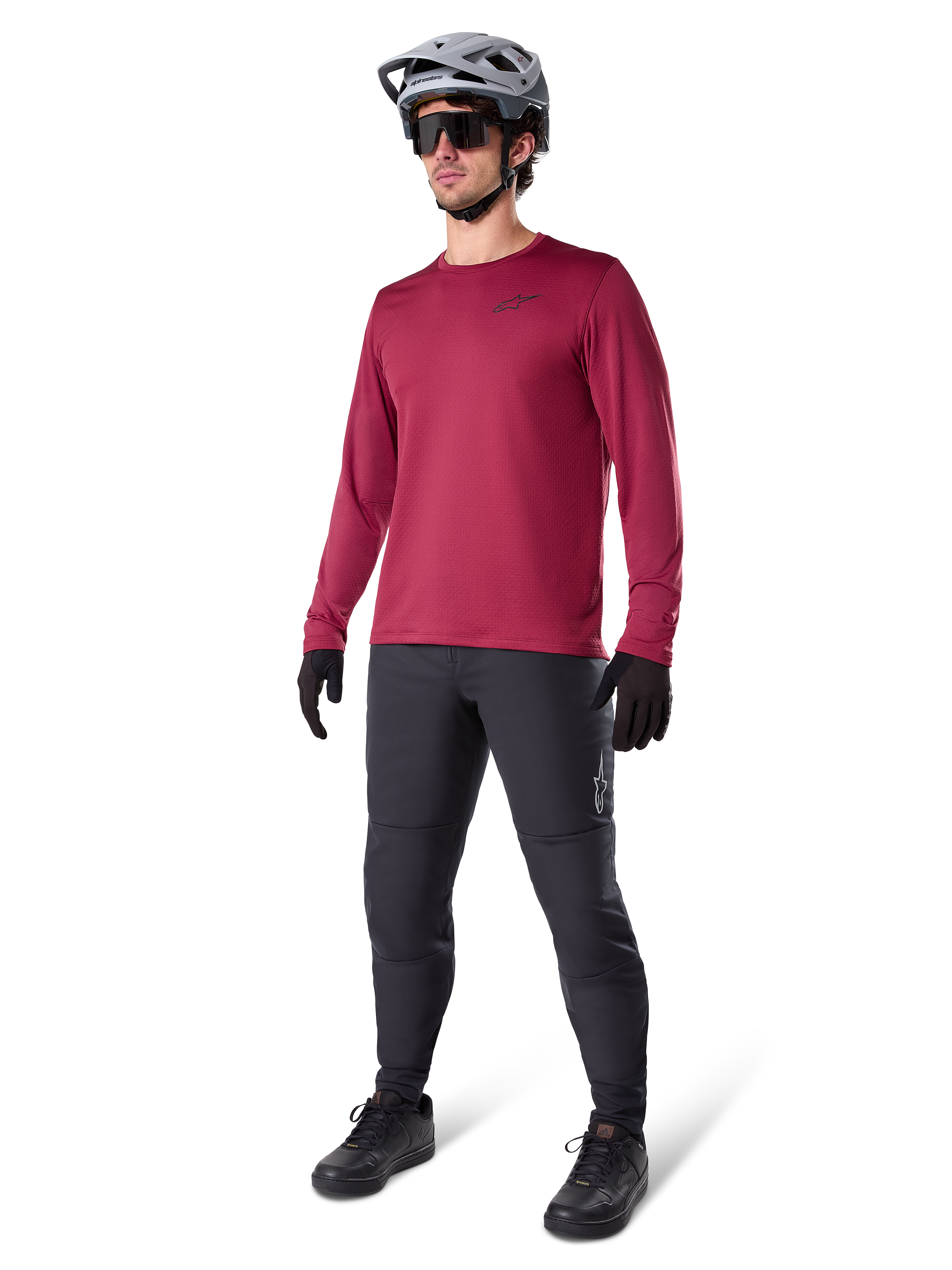 Alpinestars A-Dura Thermal Jersey i vinrött, långärmad isolerad cykeltröja bärs med mörkgrå mountainbikebyxor, svarta handskar och en grå hjälm, helkroppsbild i studio av MTB-utrustning för kallt väder.
