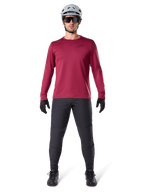 Manlig modell som bär Alpinestars A-Dura Thermal Jersey i vinrött, långärmad isolerad cykeltröja, kombinerad med mörkgrå mountainbikebyxor, vit hjälm, svarta solglasögon och svarta handskar, professionell MTB-utrustning för kallt väder