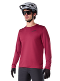 Alpinestars A-Dura Thermal Jersey, långärmad mountainbiketröja, vinröd, med isolerande fleecefoder och en liten svart logotyp på bröstet, bärs med en grå hjälm, svarta solglasögon och svarta handskar, designad för cykling i kallt väder