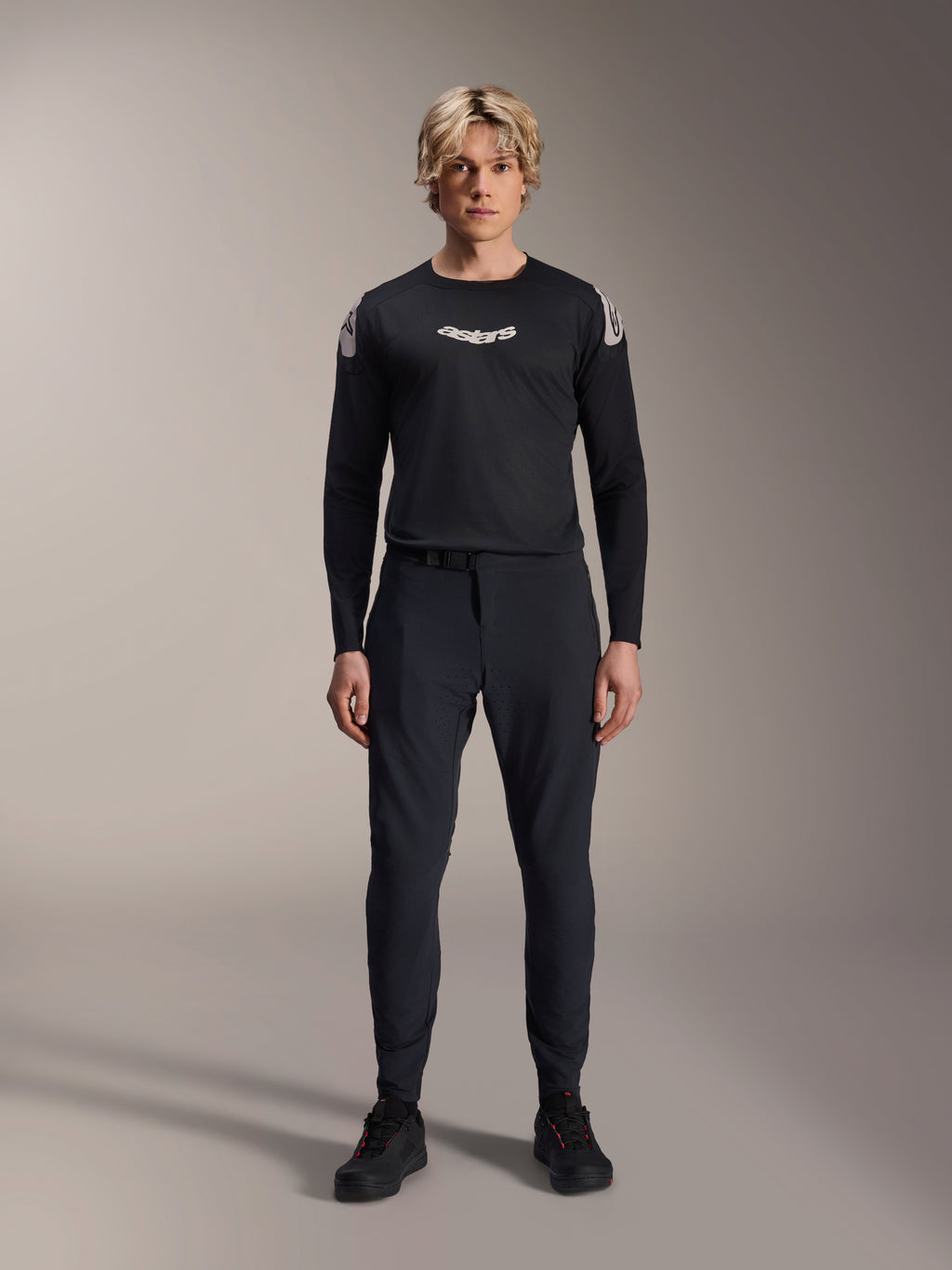 Alpinestars A-Aria Elite Pants, Black Titanium MTB Pants, worn by a male model with a matching black long-sleeve jersey and sneakers, slim-fit performance design with magnetic buckle closure, technical mountain bike apparel