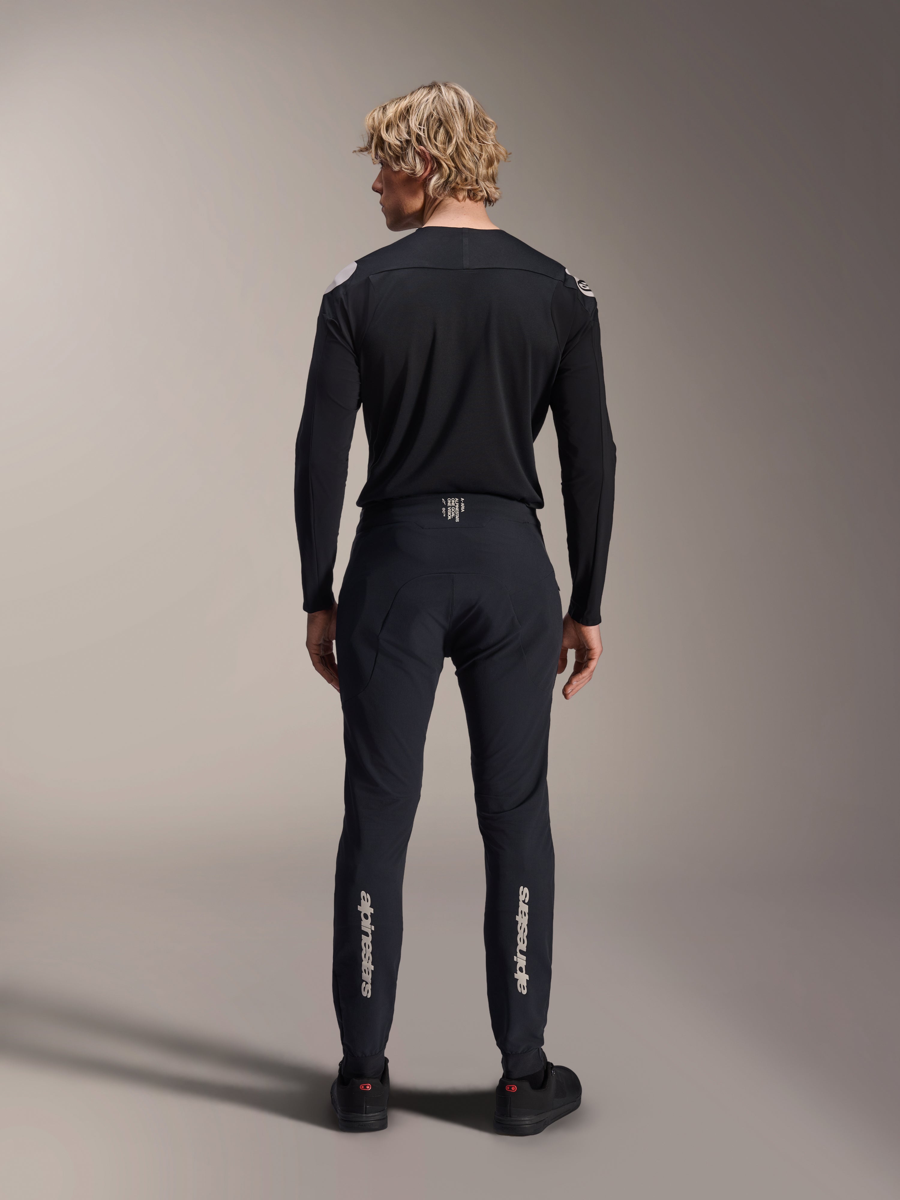 Alpinestars A-Aria Polartec Elite långärmad tröja, svart MTB-tröja, sedd bakifrån med matchande svarta byxor, prestandapassform för mountainbike, med tekniskt fukttransporterande material och diskret logotyp på nedre delen av ryggen