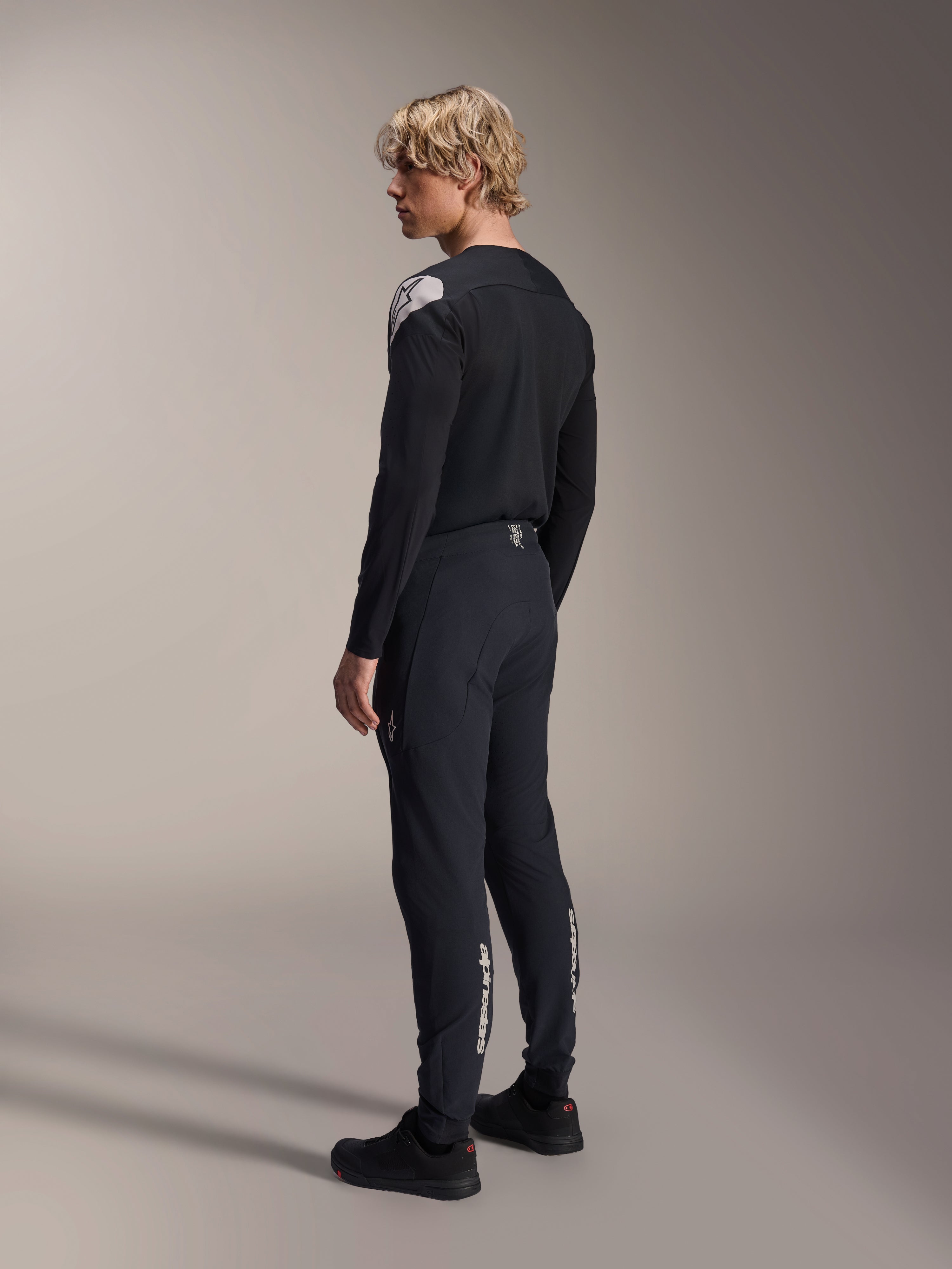 Alpinestars A-Aria Polartec Elite Jersey - långärmad, svart, buren av en modell i profil bakifrån, med en vit logotyp på axeln, kombinerad med matchande svarta cykelbyxor för en professionell MTB-outfit.
