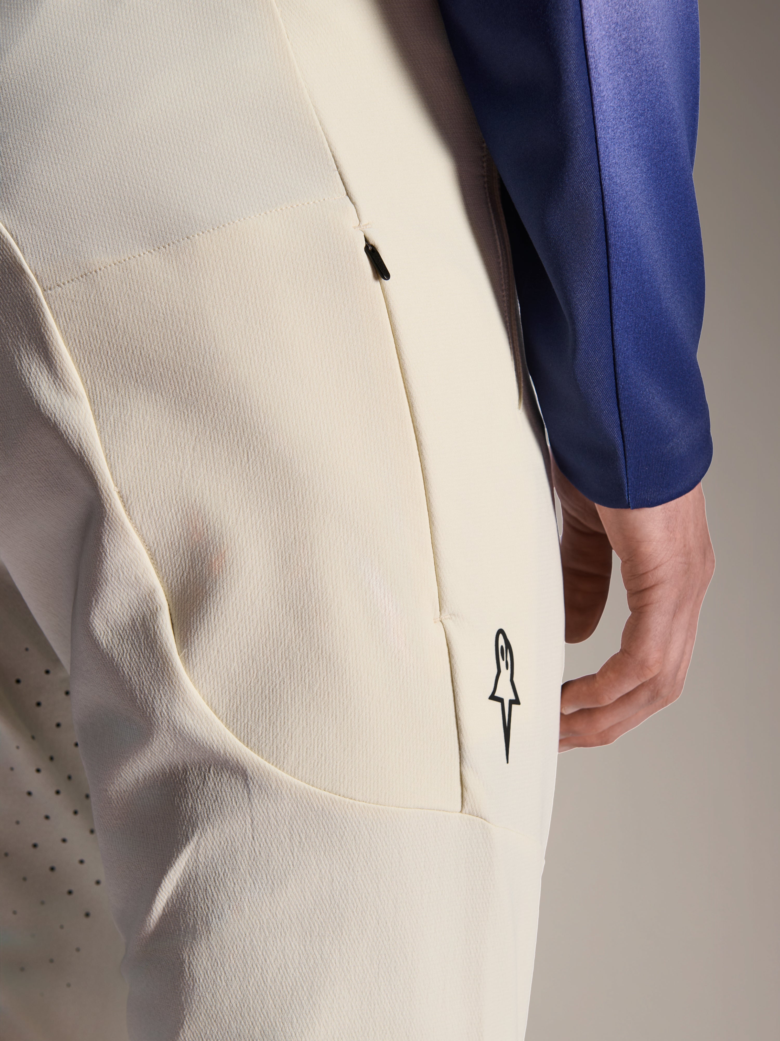 Alpinestars A-Aria Elite-byxor, Ecru off-white funktionsbyxor, närbild på sidoficka med dragkedja och laserperforeringar för ventilation, minimalistisk logotypdetalj, material med hög stretch för mountainbike