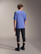 Alpinestars A-Aria Polartec Elite kortärmad tröja i Baja Blue, ryggvy på en manlig modell, kombinerad med svarta MTB-shorts och knäskydd, med prestandapassform och förlängd rygg för trailcykling.