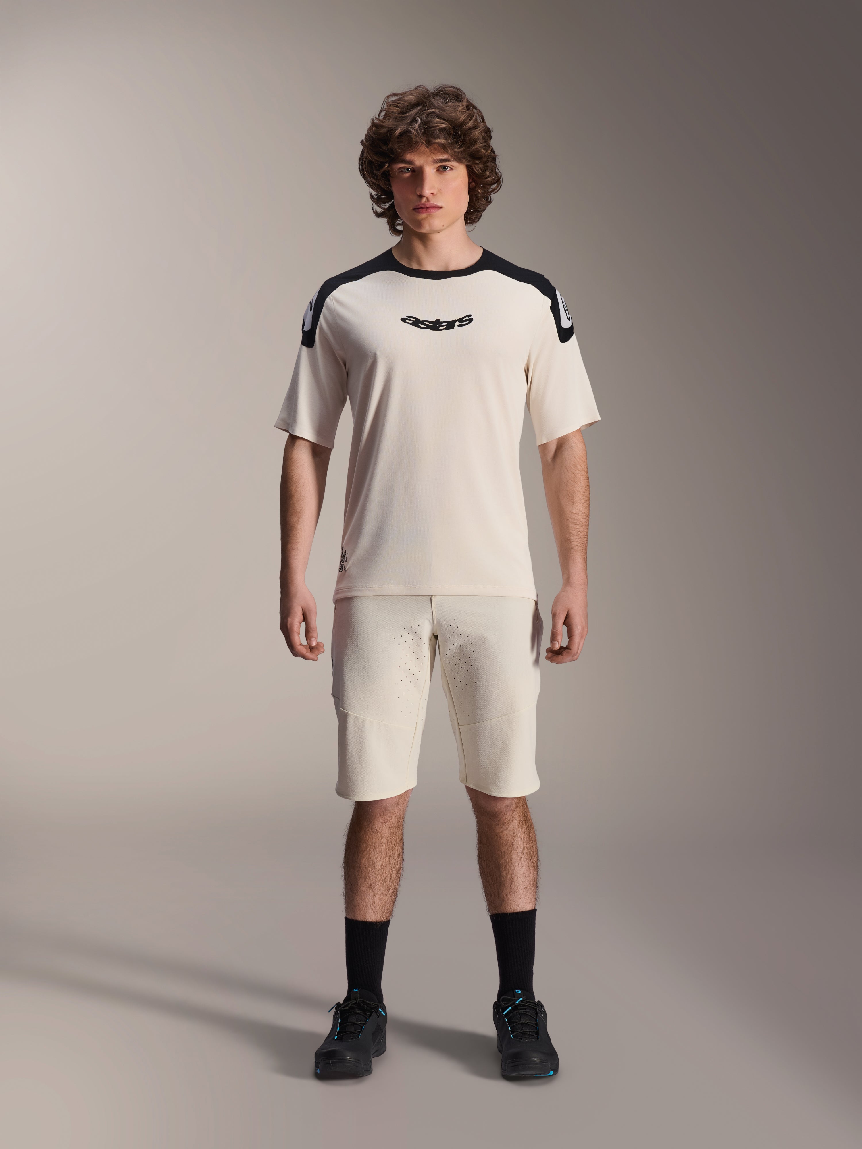Alpinestars A-Aria Polartec Elite kortärmad tröja i Ecru, med svarta axelpaneler och centrerad logotyp på bröstet, matchad med matchande ecru-shorts, svarta strumpor och cykelskor, premiumutrustning för mountainbike.
