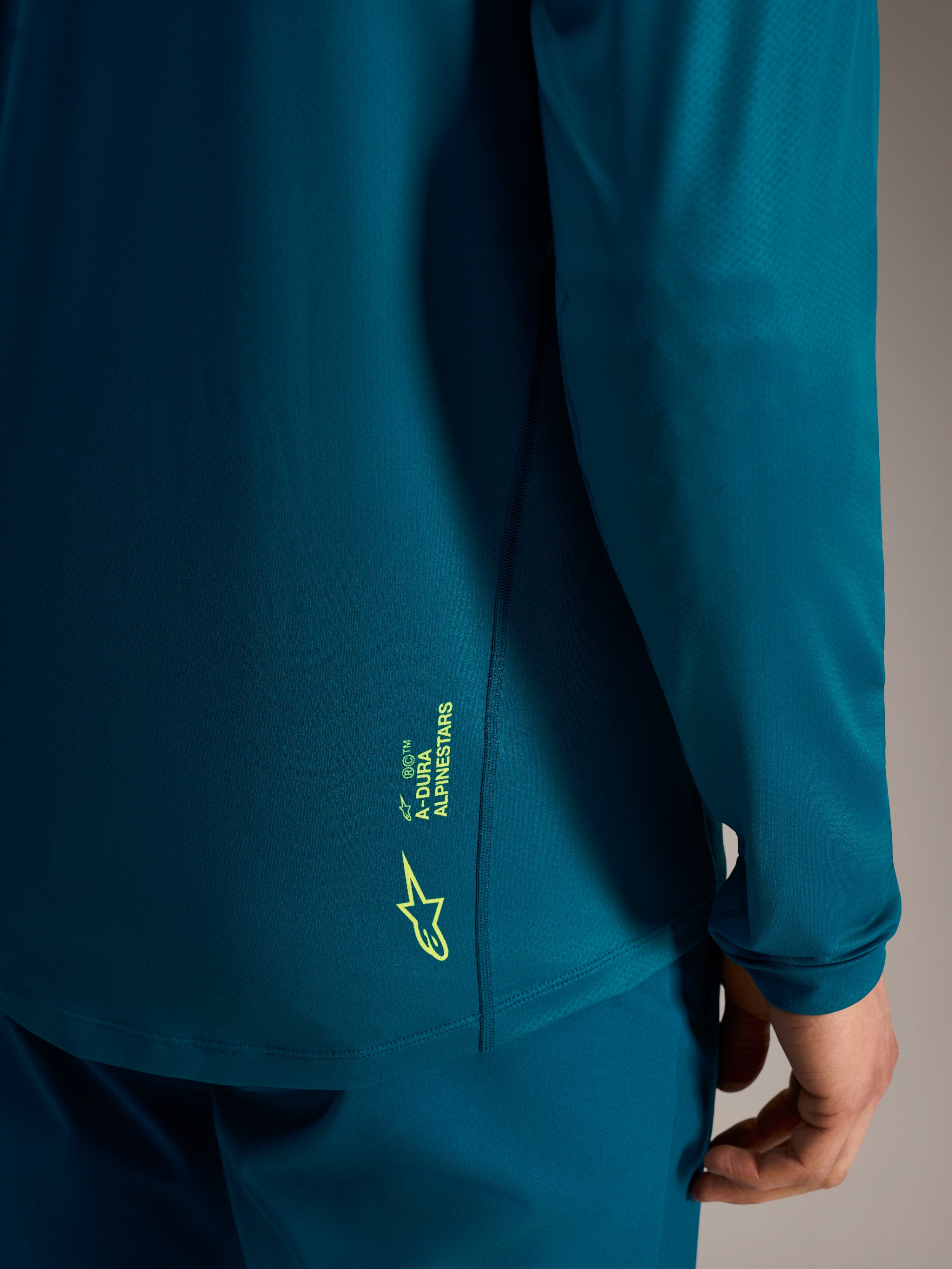 Blågrön Alpinestars A-Dura Ride långärmad tröja med limegrön logotyp på den texturerade nederkanten bak.