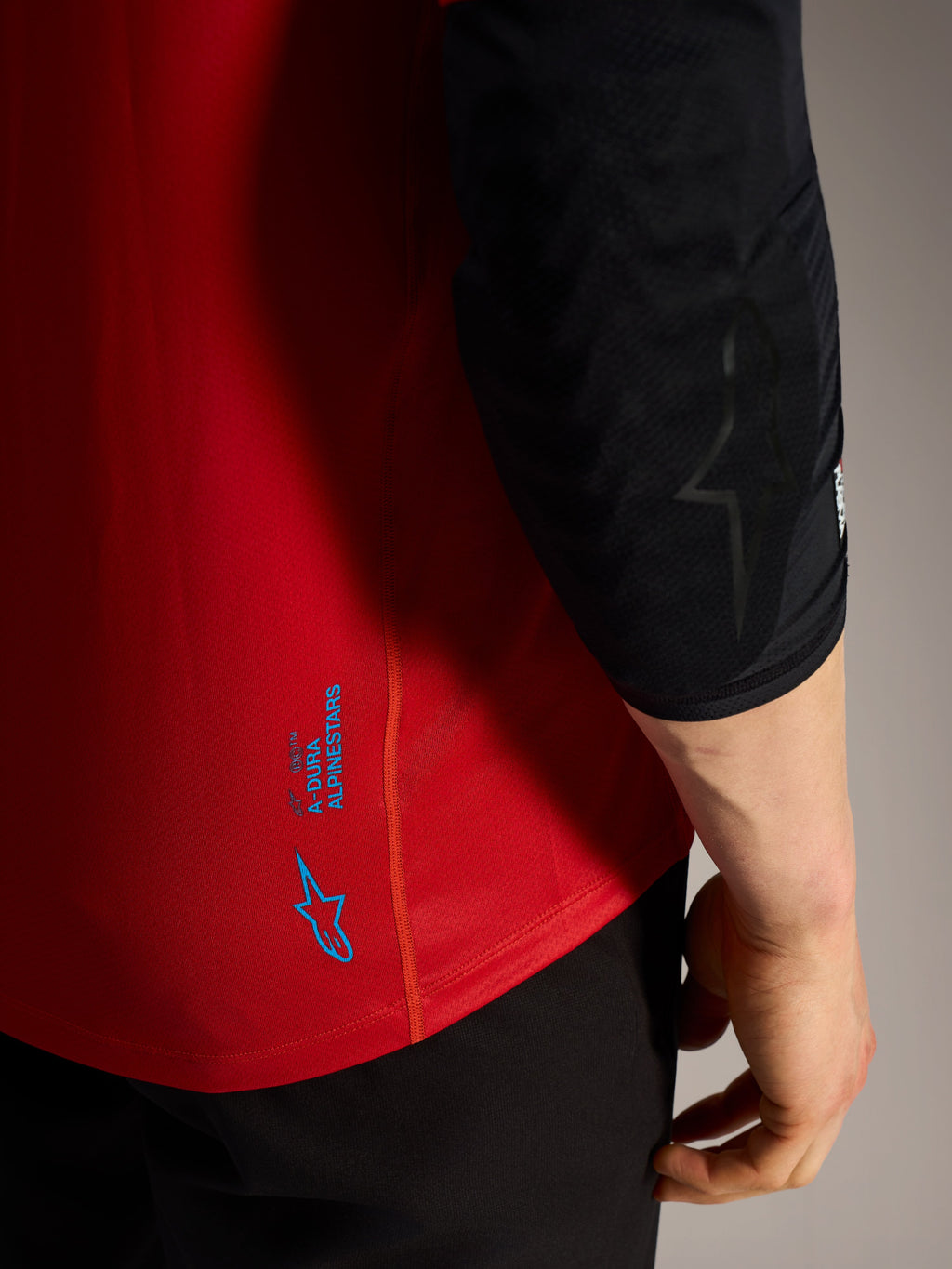 Detalj av röd Alpinestars A-Dura Ride kortärmad tröja med blå logotyper och tekniskt material för MTB.