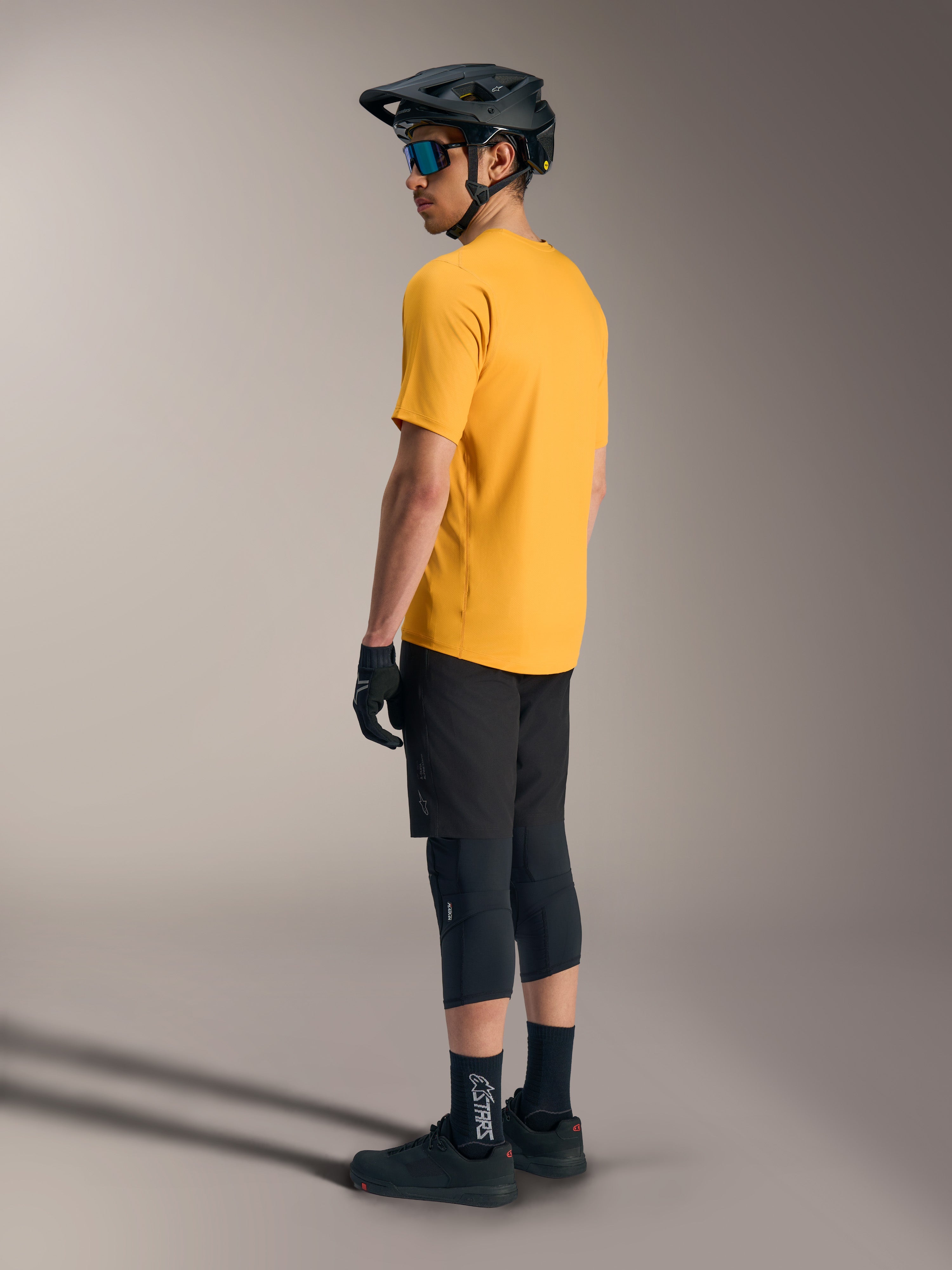 Alpinestars A-Dura Ride kortärmad tröja i orange, sedd bakifrån på en förare med svart MTB-utrustning och hjälm.