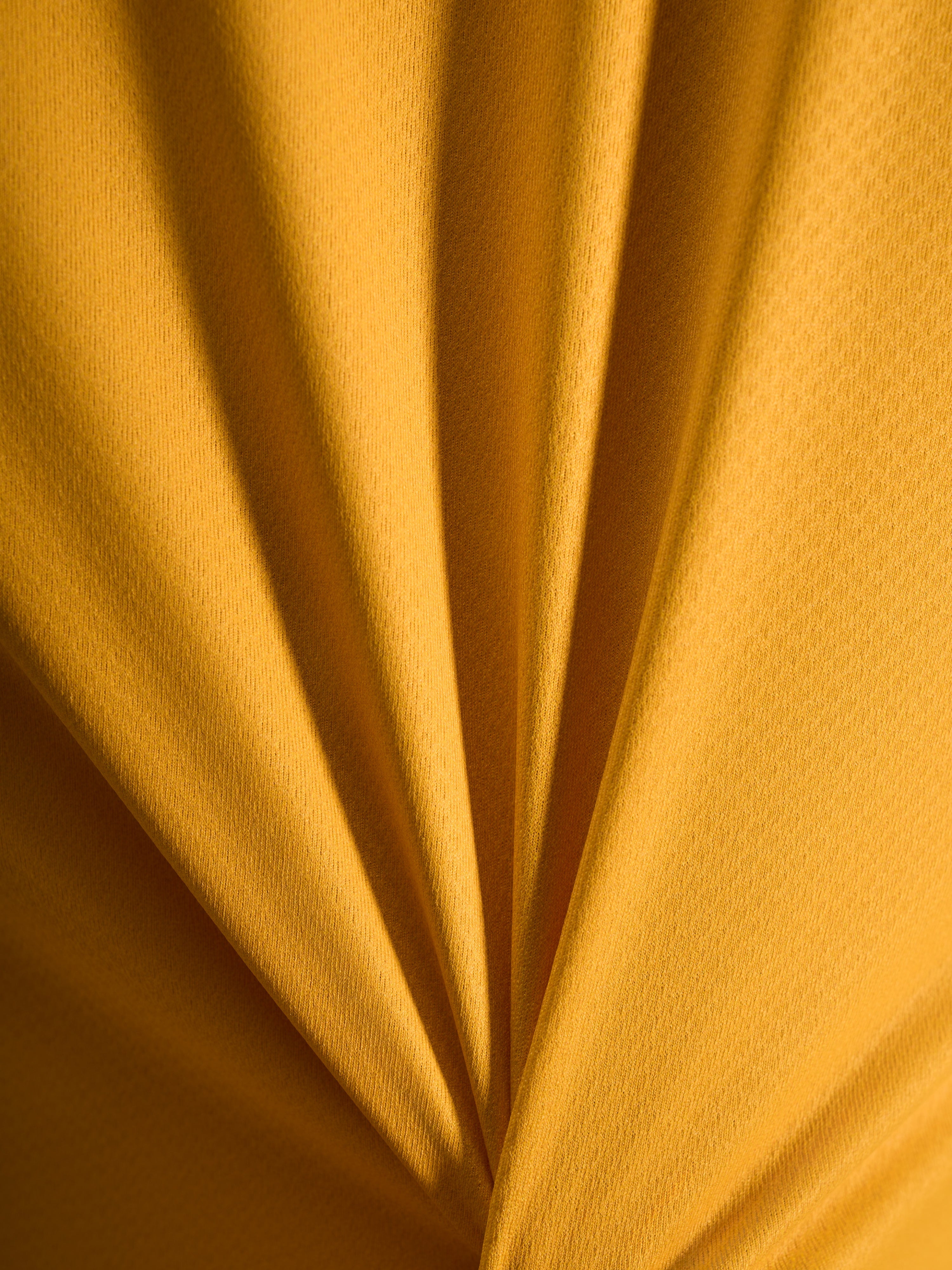 Närbild på tygstrukturen hos orange A-Dura Ride-tröja i lätt jacquardvävt poly/spandex-material.