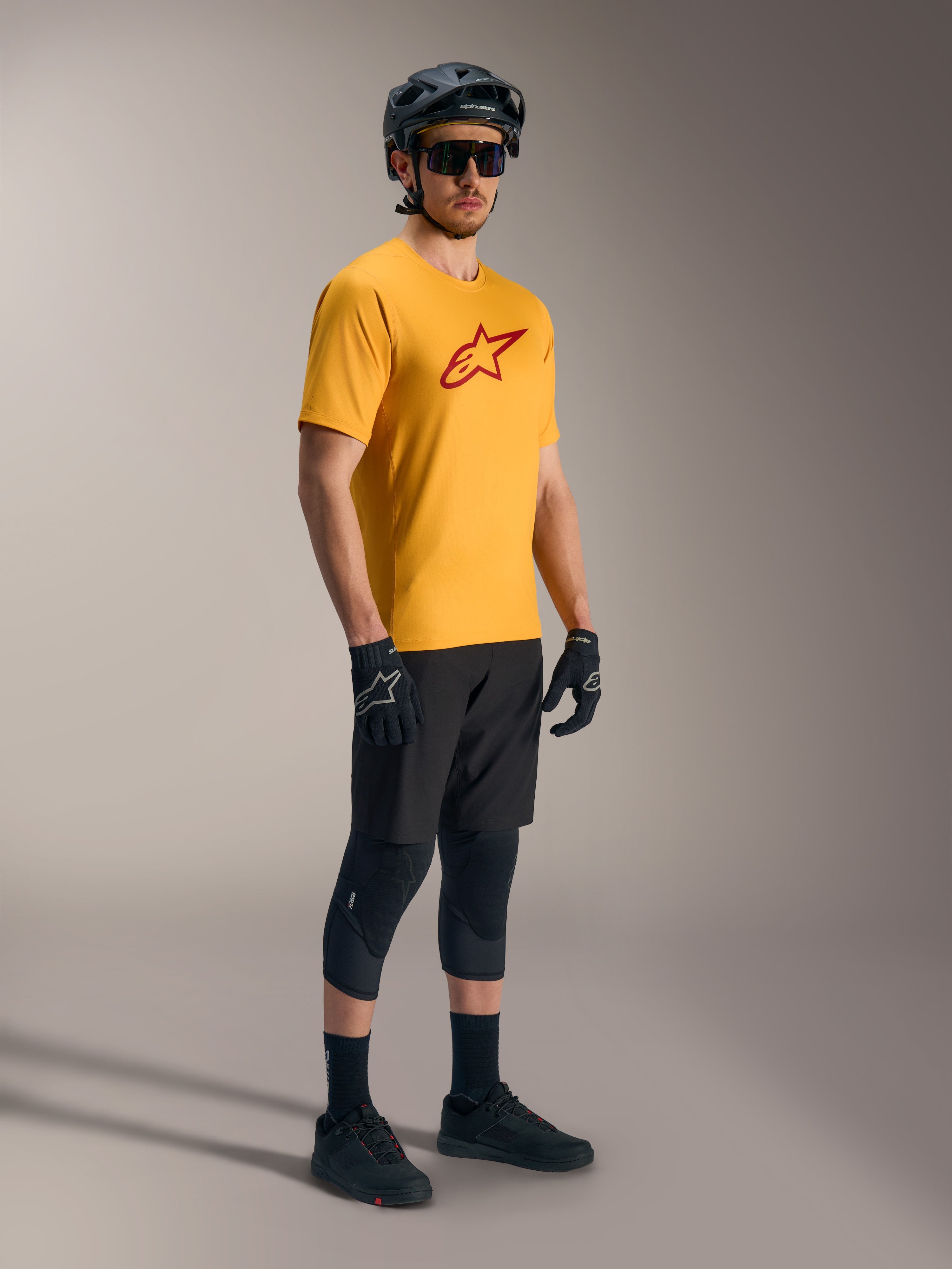Orange A-Dura Ride kortärmad tröja med röd Astars-logotyp, matchad med svart mountainbike-utrustning och hjälm.