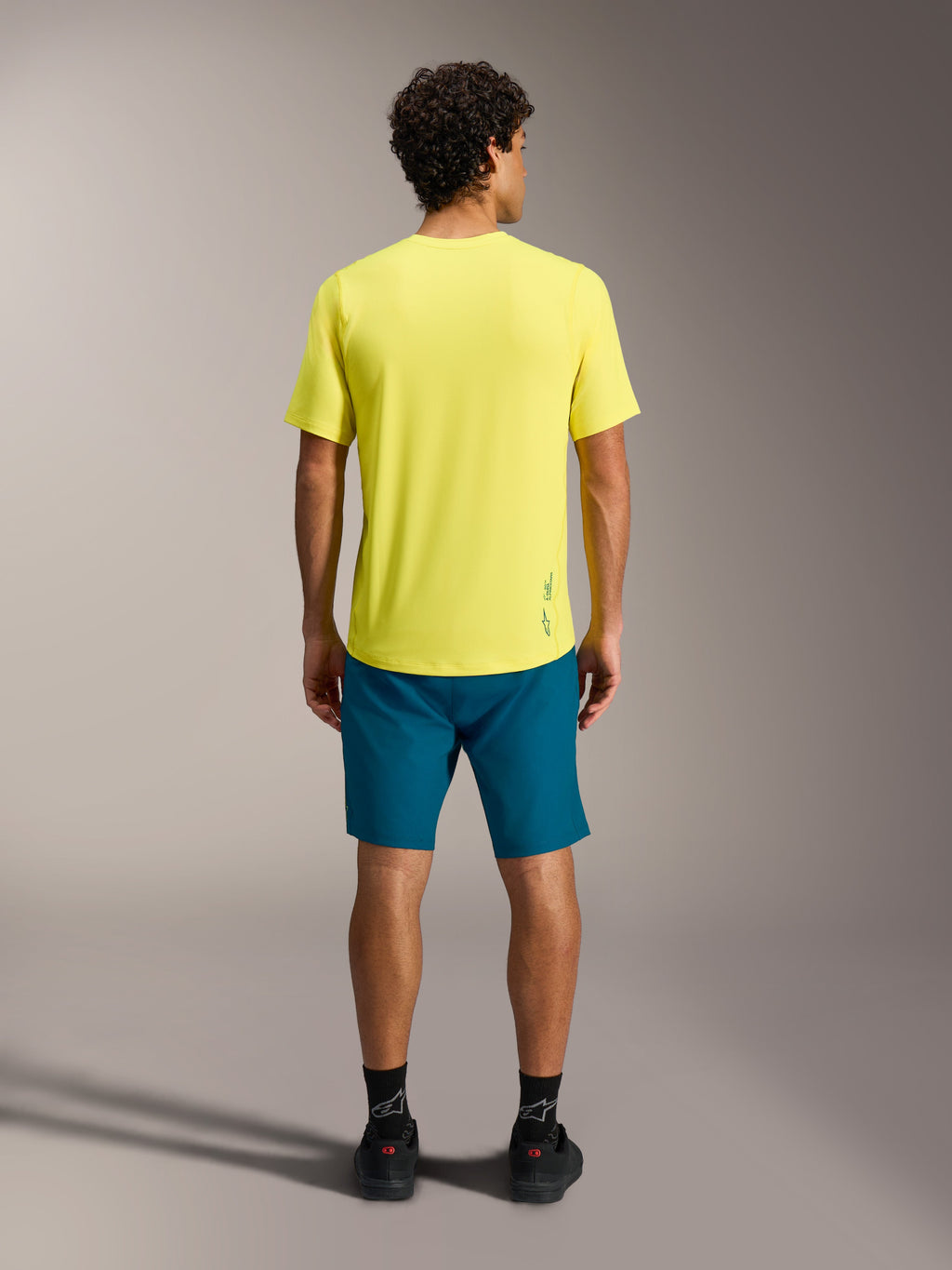 Gul A-Dura Ride SS-tröja med blågröna A-Dura Ride-shorts, sedda bakifrån, funktionell MTB-utrustning.