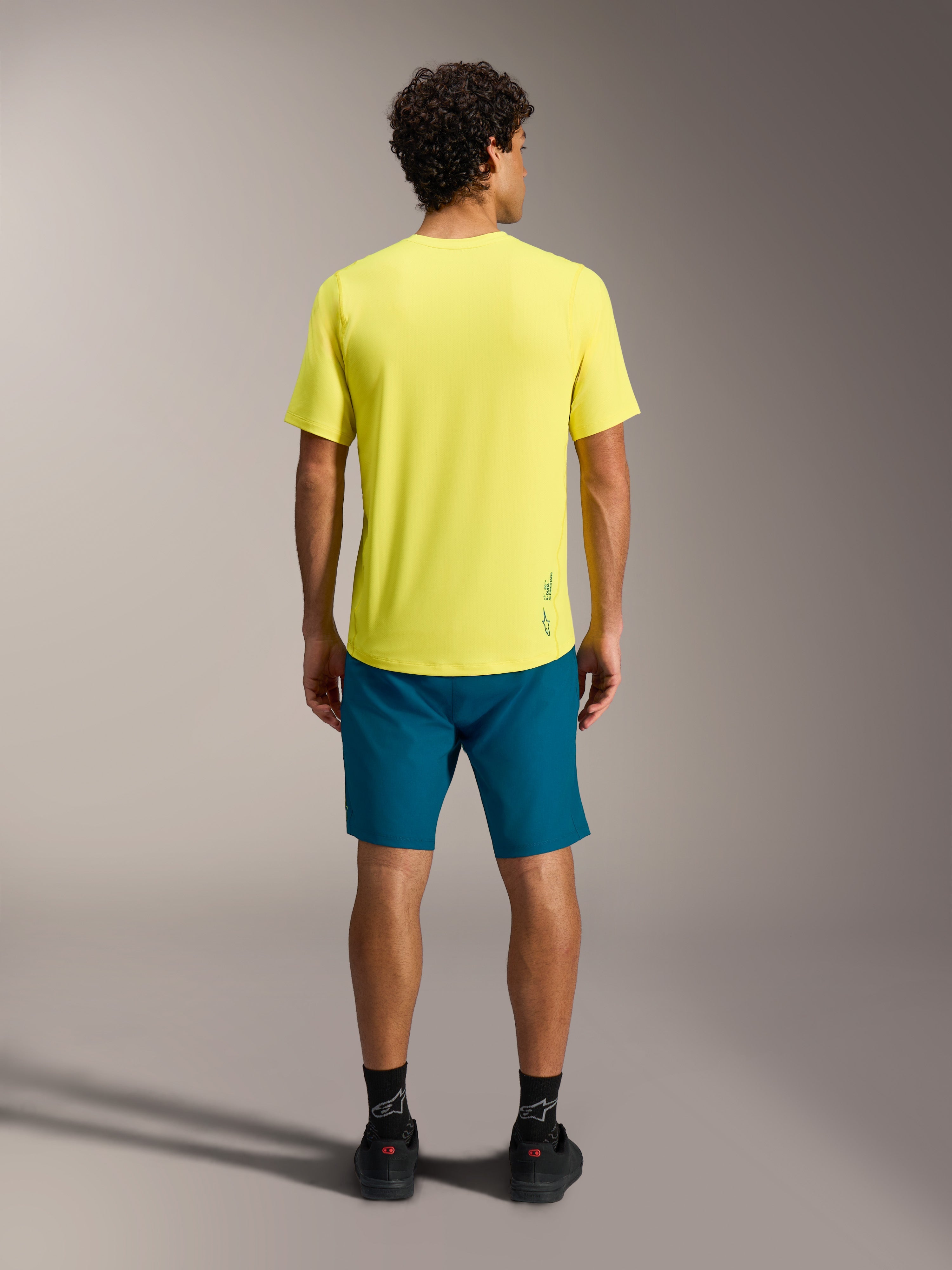 Gul A-Dura Ride SS-tröja med blågröna A-Dura Ride-shorts, sedda bakifrån, funktionell MTB-utrustning.