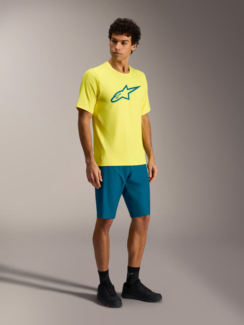 Alpinestars A-Dura Ride MTB-outfit med gul kortärmad tröja och blågröna shorts på en manlig modell.