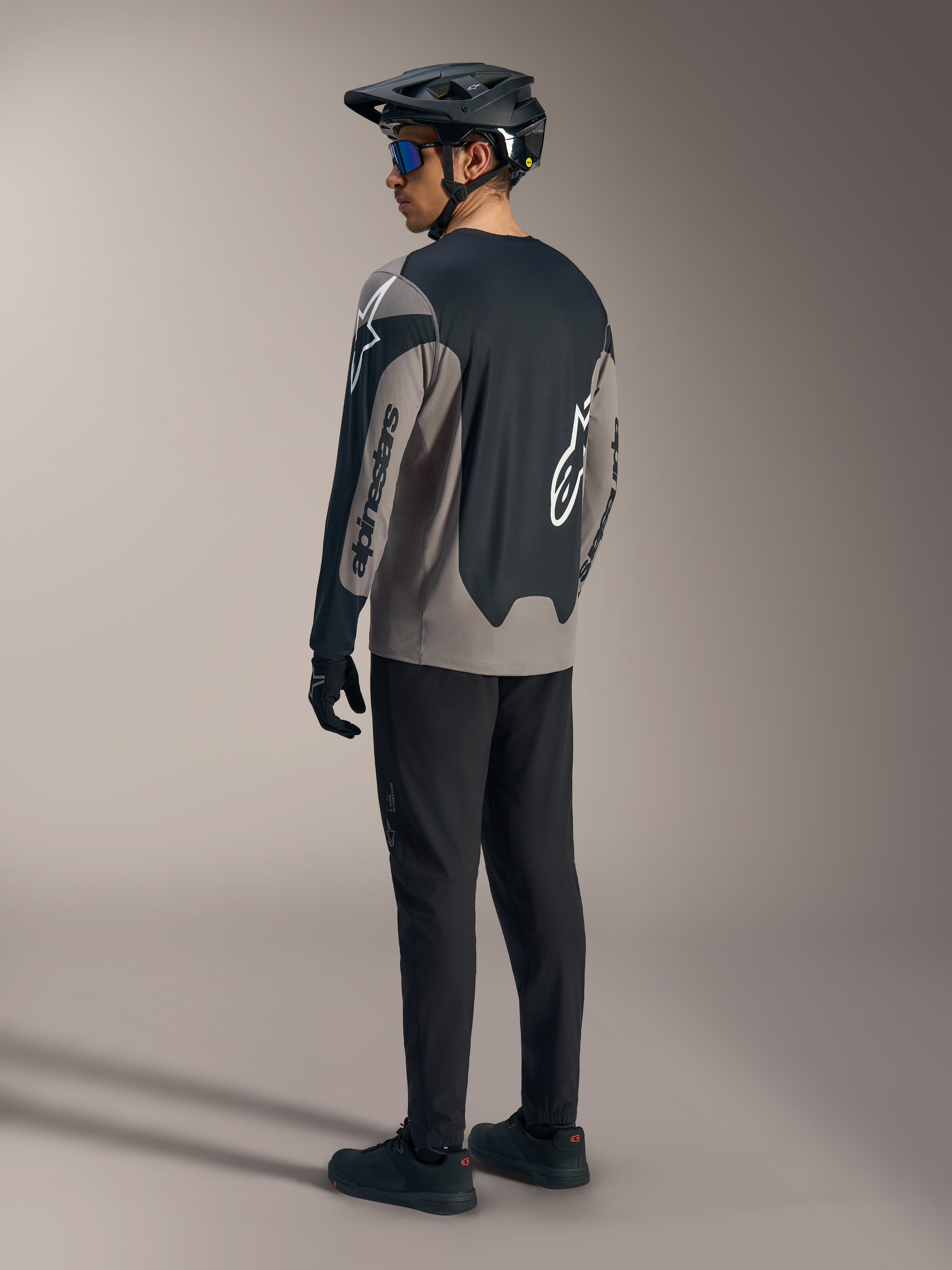 Grå och svart A-Dura Race långärmad tröja med Alpinestars-logotyper, sedd bakifrån i en komplett MTB-outfit.
