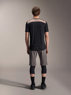 Alpinestars A-Dura Lipan tröja - kortärmad, svart med beige övre ryggpanel, vy bakifrån som visar förlängd bakdel, bärs med gråa MTB-shorts och svarta knäskydd, prestandakläder för mountainbike