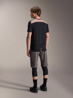 Alpinestars A-Dura Lipan kortärmad tröja i svart, ryggvy på modell som visar den ljusbruna perforerade meshpanelen över övre ryggen, kombinerad med grå mountainbikeshorts och svarta knäskydd för en komplett outfit för stigcykling.