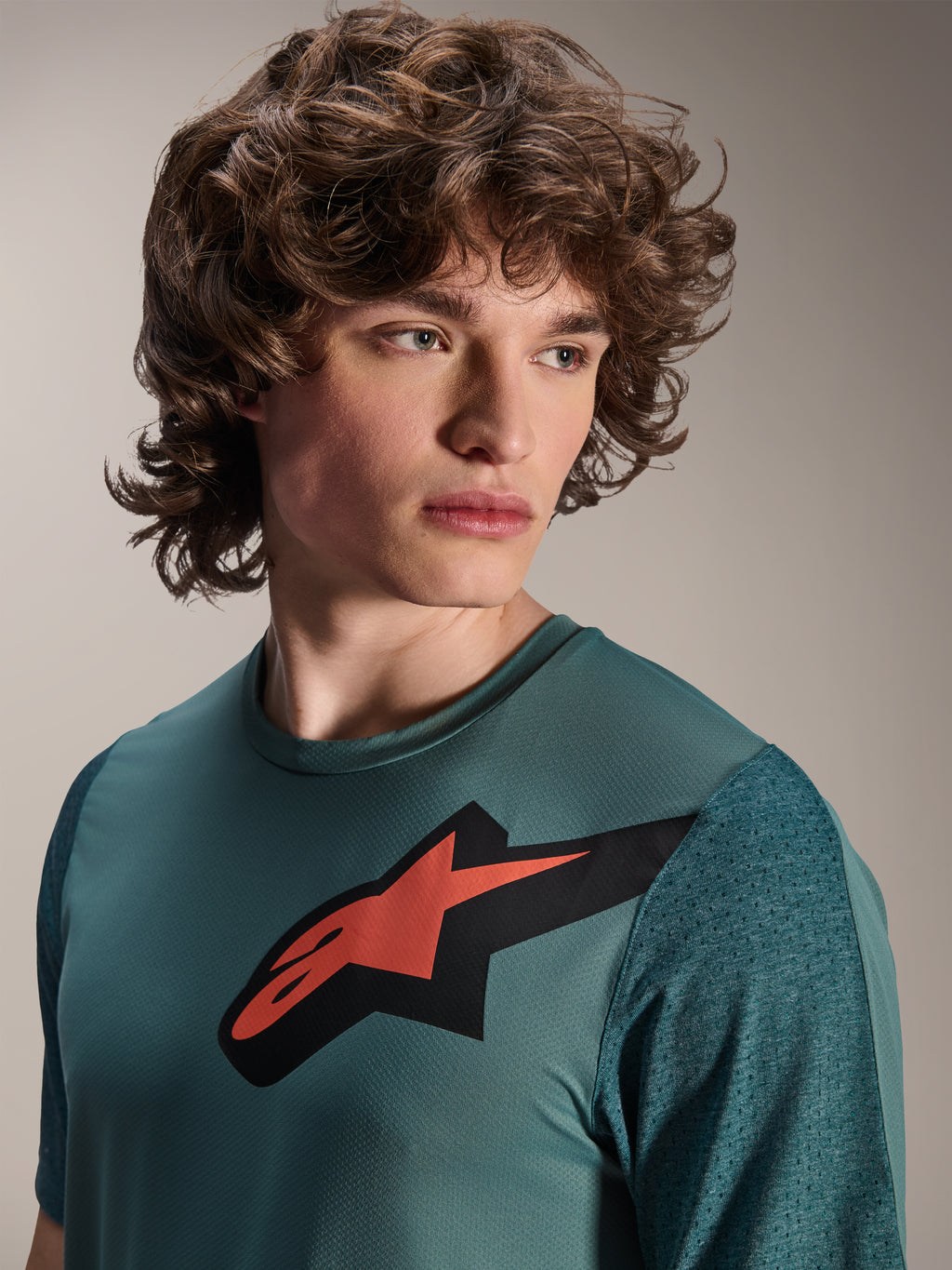 Alpinestars A-Dura Lipan-tröja, kortärmad MTB-tröja, Silver Pine, har en framträdande röd och svart Astars-logotyp på bröstet, texturerade jacquard-ärmar, närbildsporträtt av en modell klädd i högpresterande cykelutrustning