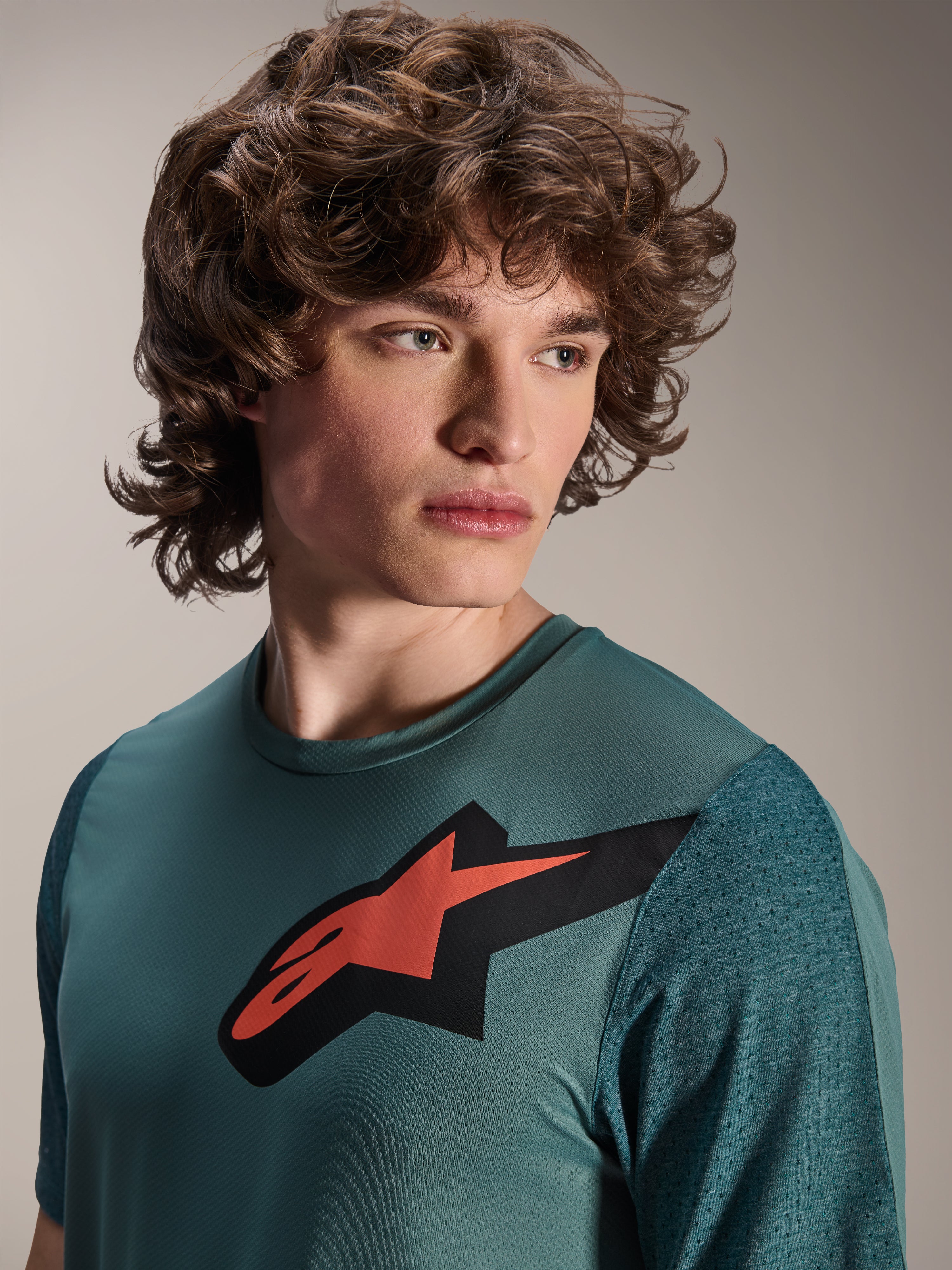 Alpinestars A-Dura Lipan-tröja, kortärmad MTB-tröja, Silver Pine, har en framträdande röd och svart Astars-logotyp på bröstet, texturerade jacquard-ärmar, närbildsporträtt av en modell klädd i högpresterande cykelutrustning