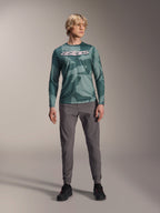 Alpinestars A-Dura Hollow Camo långärmad tröja, Silver Pine Camo med grönt kamouflagemönster, stor vit "astars"-logotyp på bröstet, bärs med grå tekniska byxor och svarta cykelskor, högpresterande MTB-utrustning
