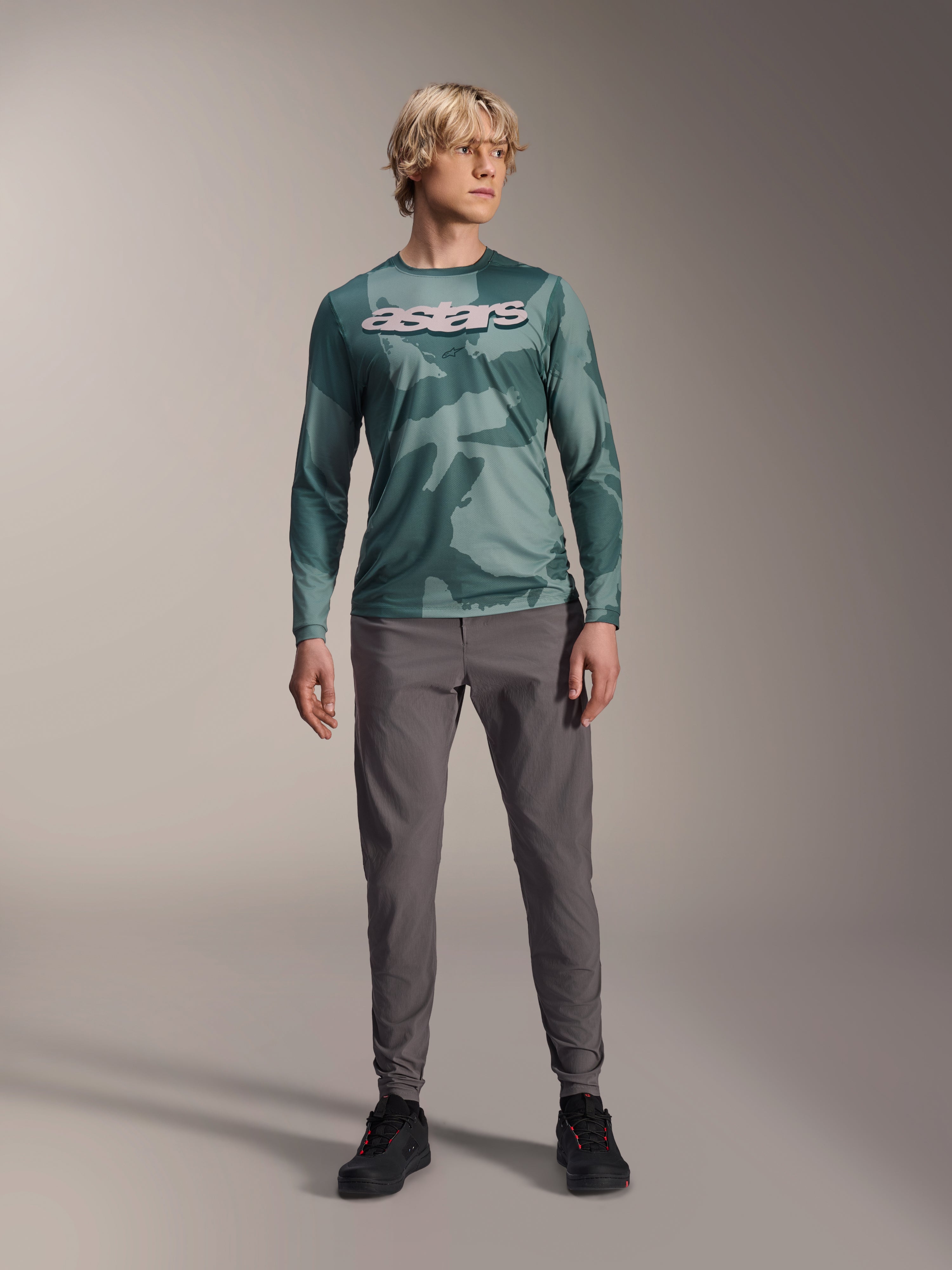 Alpinestars A-Dura Hollow Camo långärmad tröja, Silver Pine Camo med grönt kamouflagemönster, stor vit "astars"-logotyp på bröstet, bärs med grå tekniska byxor och svarta cykelskor, högpresterande MTB-utrustning