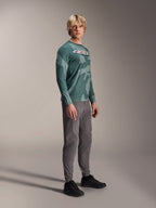 Alpinestars A-Dura Hollow Camo långärmad tröja, Silver Pine Camo, bärs av en modell med grå byxor och svarta skor, med ett grönt kamouflagemönster och en framträdande vit ASTARS-logotyp på bröstet, högpresterande MTB-kläder