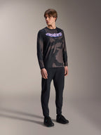 Manlig modell iklädd Alpinestars A-Dura Hollow Camo långärmad tröja, Black Camo-mönster med lila 'astars'-grafik på bröstet, kombinerat med svarta tekniska byxor och svarta skor, avslappnad MTB-utrustning
