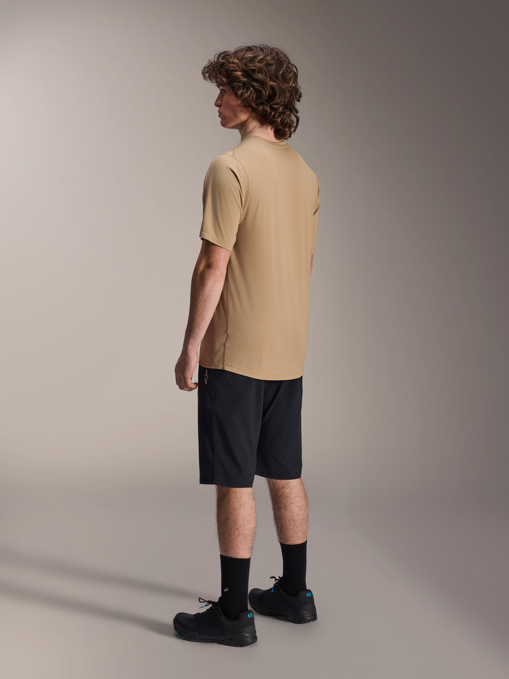 Alpinestars A-Dura Liner Shorts i svart och A-Dura SS Jersey i beige, bärs av en manlig modell sedd från sidan, matchade med svarta strumpor och cykelskor, livsstilskläder för mountainbike