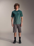 Manlig modell i Alpinestars A-Dura Rise kortärmad tröja i Silver Pine, grön cykeltröja med liten vit logotyp på bröstet, matchad med grå mountainbikeshorts och svarta skor, avslappnad MTB-utrustning