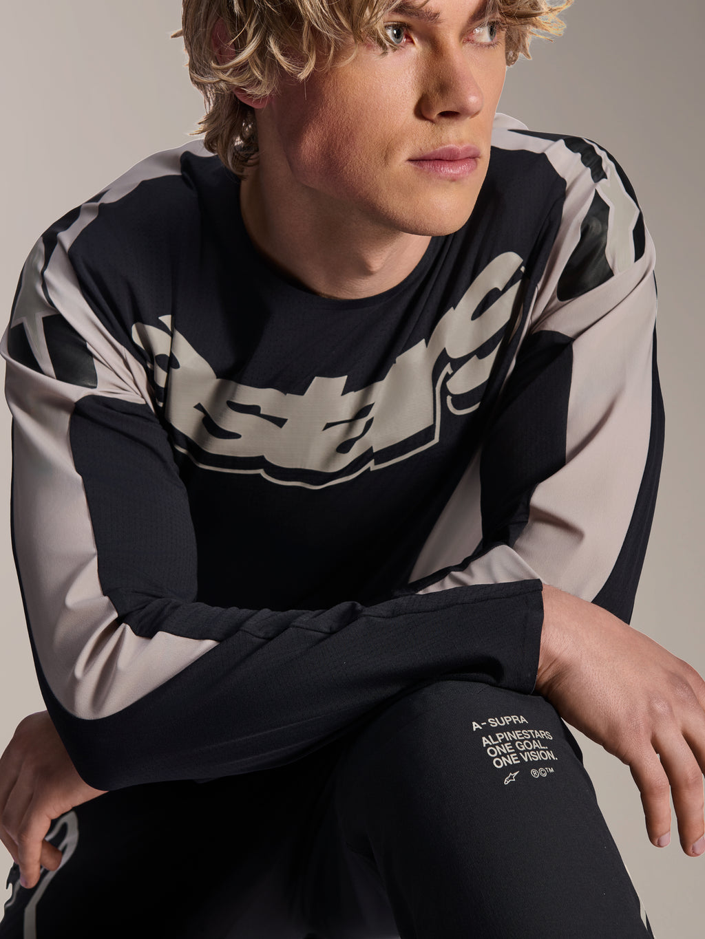 Alpinestars A-Supra Melt-tröja, långärmad MTB-tröja, svart med ljusgrå grafik, bärs av modell, med stor logotyp på bröstet och 'One Goal. One Vision.'-detaljer, funktionella mountainbikekläder