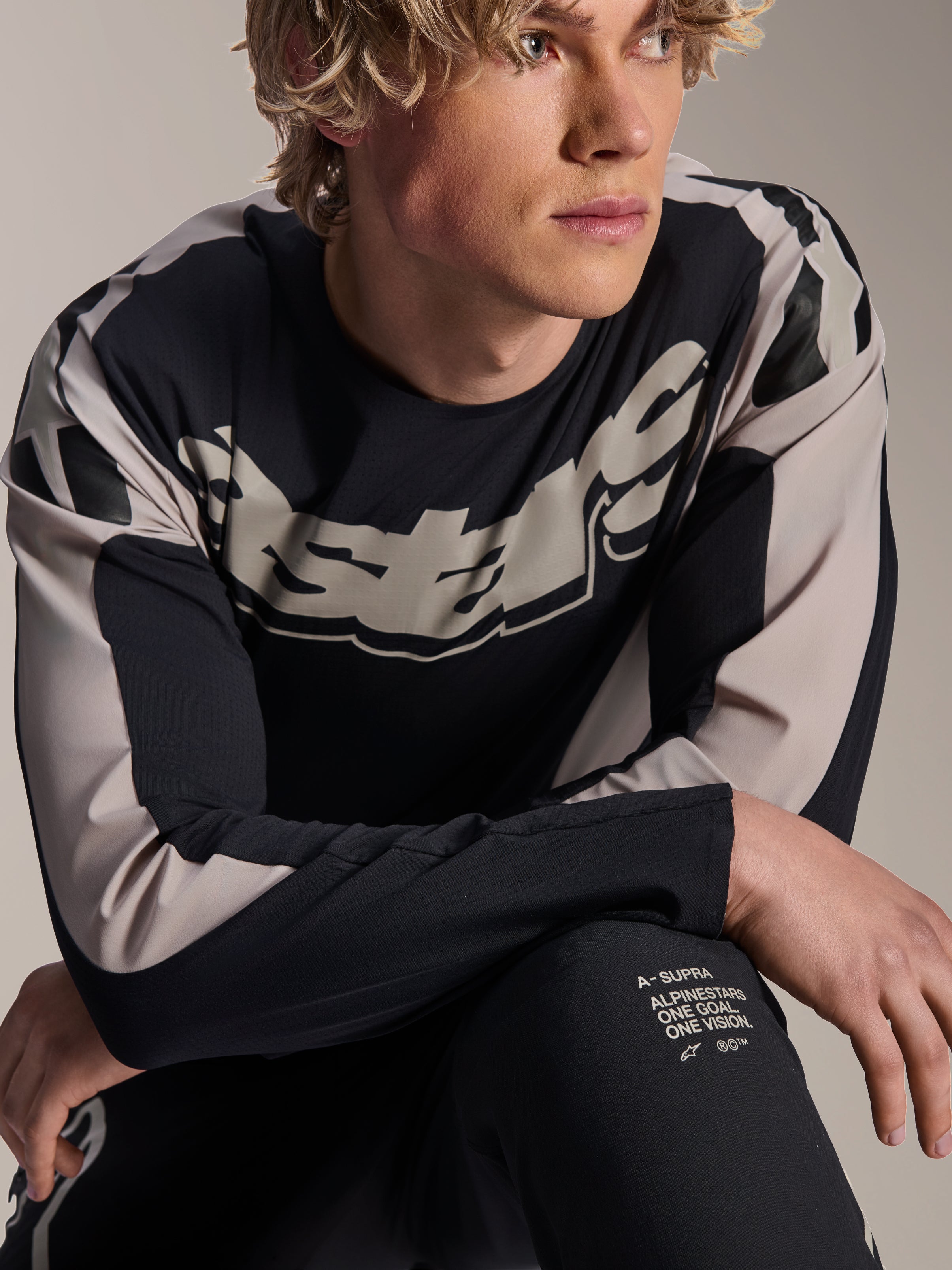 Alpinestars A-Supra Melt-tröja, långärmad MTB-tröja, svart med ljusgrå grafik, bärs av modell, med stor logotyp på bröstet och 'One Goal. One Vision.'-detaljer, funktionella mountainbikekläder