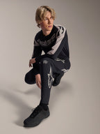 Alpinestars A-Supra Melt-byxor och långärmad tröja, svarta och grå, med framträdande vit branding och stjärnlogotyper, buren av en manlig modell i en hukande pose, matchande MTB-racingutrustning