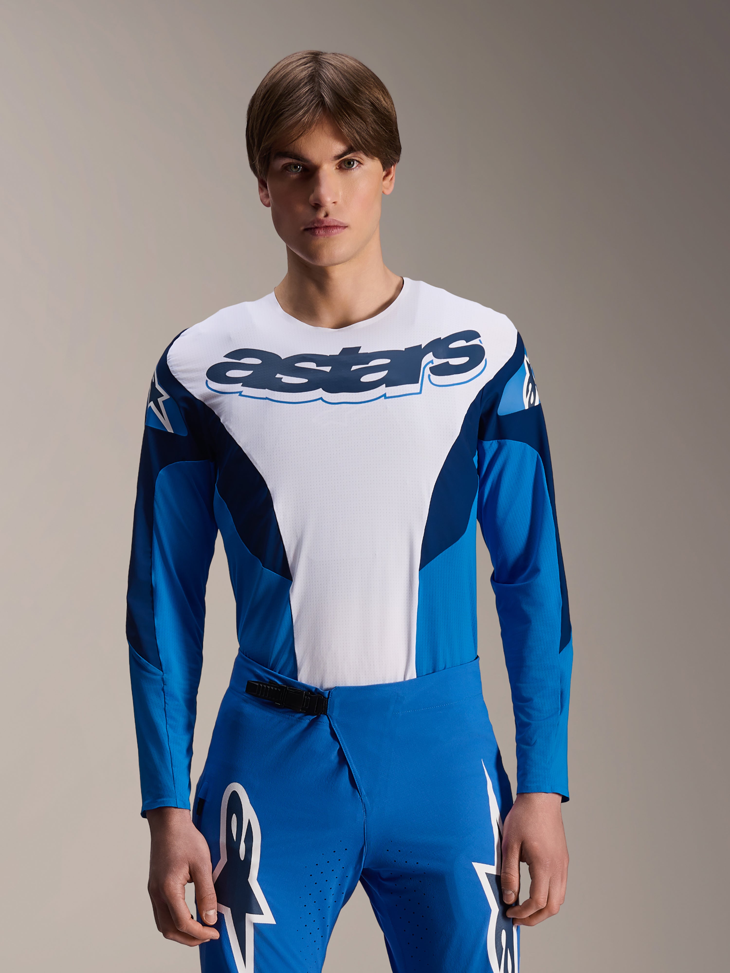 Alpinestars A-Supra Melt långärmad tröja, blå och vit MTB-tröja, med tydlig astars-logotyp över bröstet och mörkblå ärmar, bärs med matchande blå racingbyxor med vita stjärnlogotyper, högpresterande mountainbike-kläder