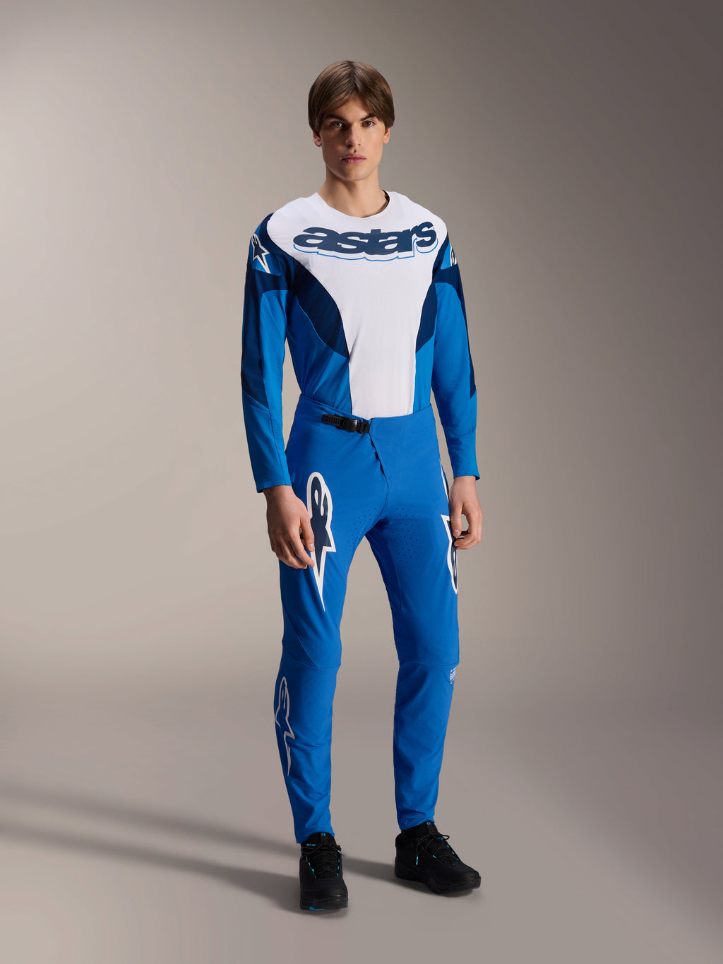 Modell i komplett Alpinestars MTB-racingutrustning, blå och vit långärmad tröja med 'astars'-logotyp, matchande blå A-Supra Melt-byxor med vita stjärnlogotyper, professionella mountainbikekläder för terrängkörning