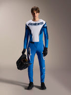 Manlig cyklist bär Alpinestars A-Supra Melt långärmad tröja i blått och vitt, med 'astars'-branding på bröstet, matchande blå byxor, svarta handskar och håller en svart hjälm, prestationsfokuserat MTB-racingställ.