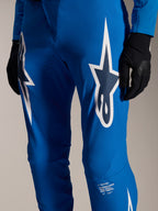 Alpinestars A-Supra Melt byxor, blå cykelbyxor med stora vita Astars-logotyper på låren, laserperforeringar för luftflöde och signaturmärkning på underbenet, bärs med svarta handskar, prestanda-MTB-utrustning